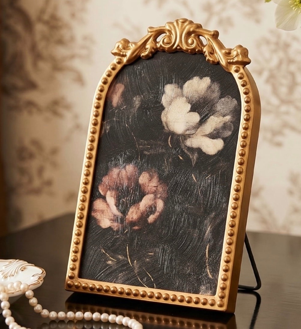 Ornate Antique Gold Frame - Intricately crafted gold metal frame with scrollwork and beaded detailing delivers timeless vintage elegance.
	•	Moody Floral Artwork - Features rich red, white, and blush roses on a deep black background for a dramatic and romantic aesthetic.
	•	Crystex Textured Finish - Light Crystex coating enhances the artwork with a subtle brushstroke texture while eliminating the need for glass.
	•	Sturdy Easel Back Display - Includes a durable metal easel stand for easy placement on shelves, desks, mantels, and other surfaces .
	•	Compact & Versatile Decorative Accent - 6x8 size is perfect for small spaces and complements a wide range of décor styles from vintage to dark academ

#LTKSeasonal #LTKHome