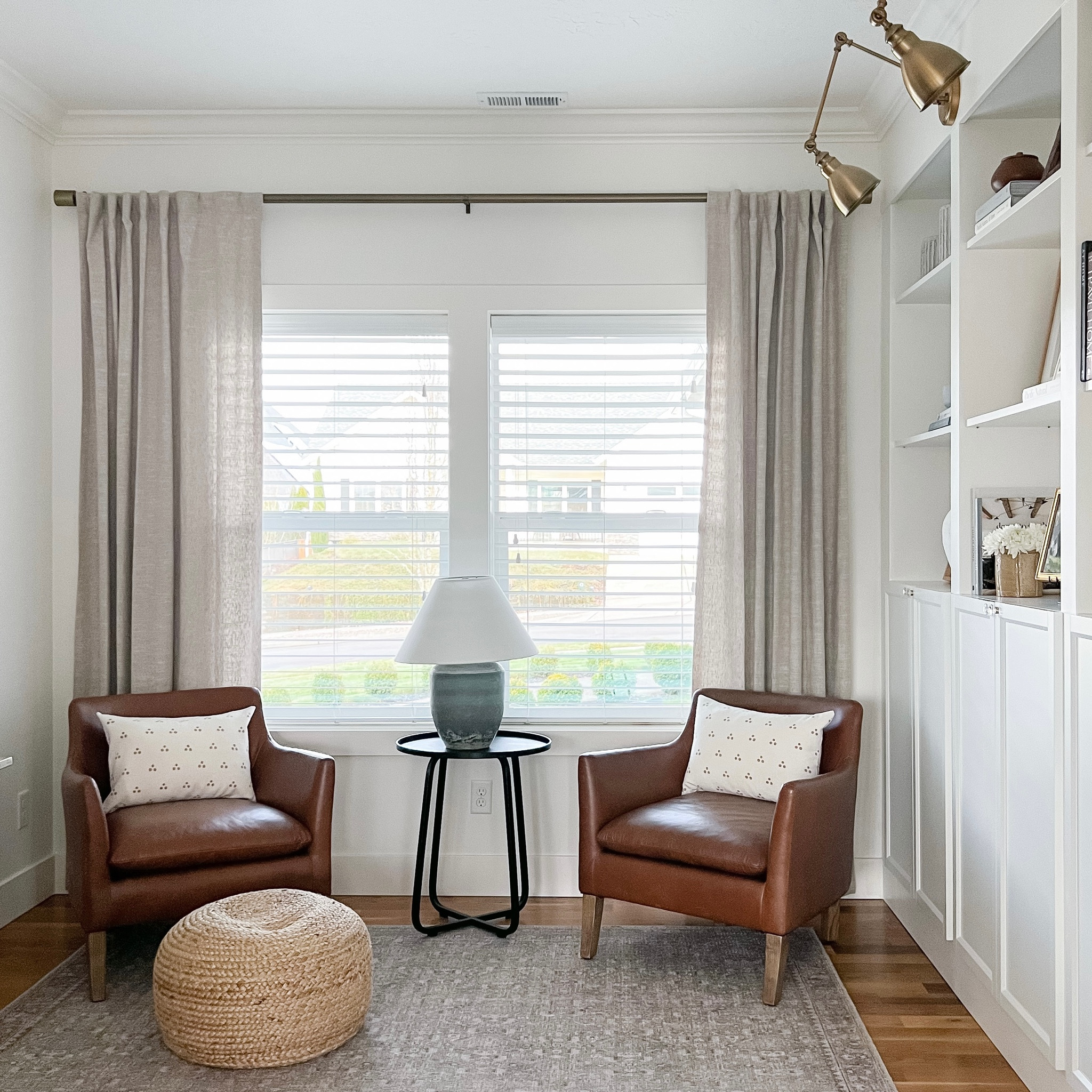 The leather chairs in my office with a black side table, table lamp, woven pouf and area rug