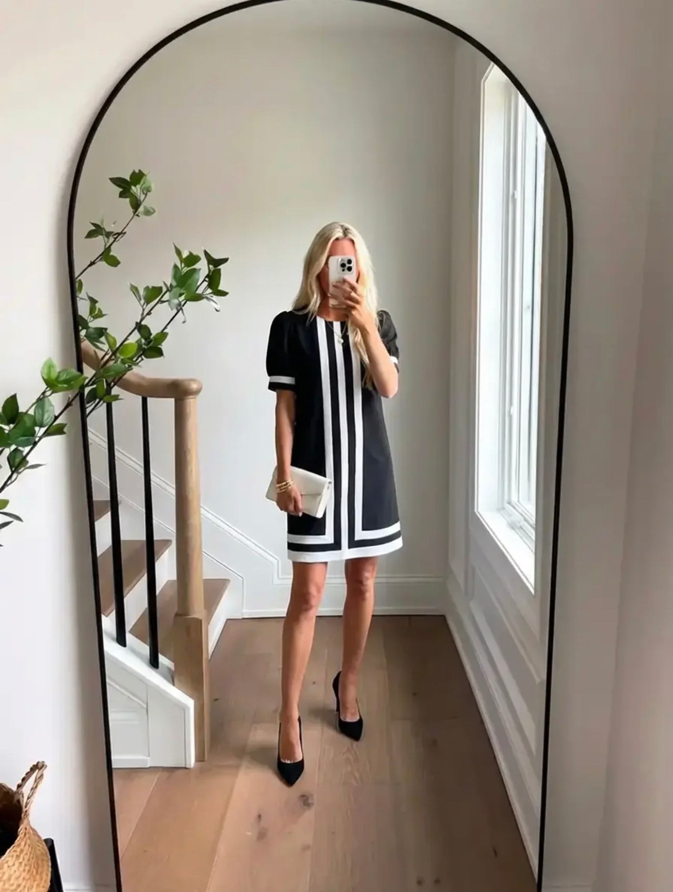 A polished lifestyle fashion mirror selfie in a bright modern home. A woman with long blonde hair stands in front of a tall arched black-framed mirror. She is wearing a chic black shift dress with bold white geometric trim and short sleeves, styled with black pointed-toe heels and a small neutral clutch. The interior features light natural oak flooring, white walls, a staircase with a light wood handrail and black metal balusters, and soft daylight streaming through a tall window. A leafy green branch adds an organic touch. The aesthetic is classic elegance, Parisian-inspired style, timeless black and white fashion, quiet luxury lifestyle photography, clean minimal interior.

⸻

Caption

Black and white never misses. Timeless for a reason. 🖤

⸻

Hashtags

#ClassicStyle
#BlackAndWhiteStyle
#TimelessFashion
#ParisianStyle
#ChicStyle
#ElegantStyle
#MinimalStyle
#OOTDInspo
#EffortlessStyle
#ClassicWardrobe
#ModernElegance
#QuietLuxury
#StyleInspoDaily
#MirrorSelfieStyle
#ChicAndSimple
#EverydayElegance
#StyleInfluencer
#CasualLuxury
#ClassicOutfit
#TimelessWardrobe


#LTKSpringSale #LTKgrwm #LTKdayinmylife