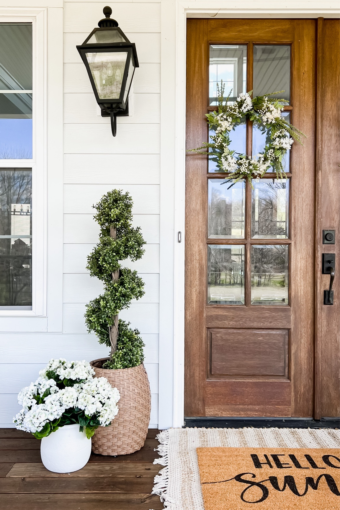 Front porch and front door, spring decor, outdoor wall, sconce lantern, gas lighting, light fixtures, floral, spring wreaths, green and yellow spiral boxwood topiary, artificial tree, geranium, hydrangeas, white wicker table, outdoor planter resin rattan, double layered doormat, and Yates got a rug, modern farmhouse style

#LTKhome #LTKFind #LTKSeasonal