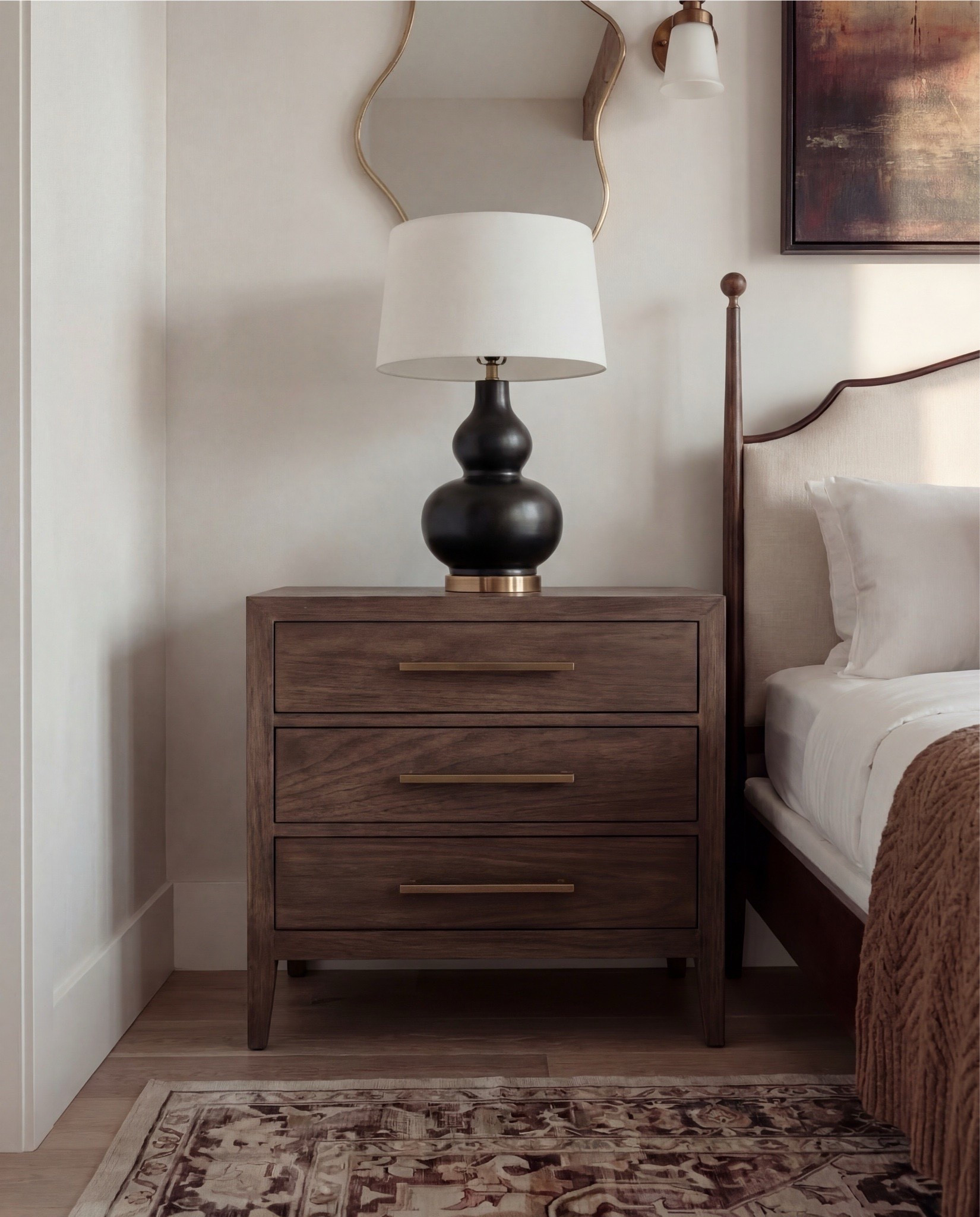 Shop the Look: Bedroom Refresh
This bedroom feels warm, grounded, and quietly elevated. The exposed wood ceiling beams bring architectural character, while the soft neutral walls and layered textiles keep everything calm and timeless. The dark wood bed frame anchors the space, balanced by creamy bedding, warm brown pillows, and a textured throw that adds just the right amount of coziness.

The mix of brass accents, sculptural lighting, and vintage-inspired details gives the room depth without feeling heavy. From the patterned area rug underfoot to the styled dresser moment with books, bowls, and dried branches, every piece feels intentional but lived-in.

Shop the Look:
• Dark wood bed frame with curved headboard
• Crisp white bedding set (duvet + sheets)
• Warm brown accent pillows
• Textured knit or woven throw blanket (camel/brown)
• Ivory boucle bench stools (set of two)
• Vintage-style patterned area rug (neutral brown + taupe tones)
• Wood nightstands with drawers
• Table lamps with white drum shades
• Wall sconces with brass detail
• Framed landscape artwork above bed
• Organic-shaped wall mirrors (brass frame)
• Black fluted dresser with brass hardware
• Round brass wall mirror
• Sculptural white ceramic bowl
• Decorative books with wood bead garland
• Neutral ceramic vase with dried branches
• Upholstered accent chair (cream fabric, wood frame)
• Slim brass floor lamp with white shade

#LTKHome #LTKSaleAlert
