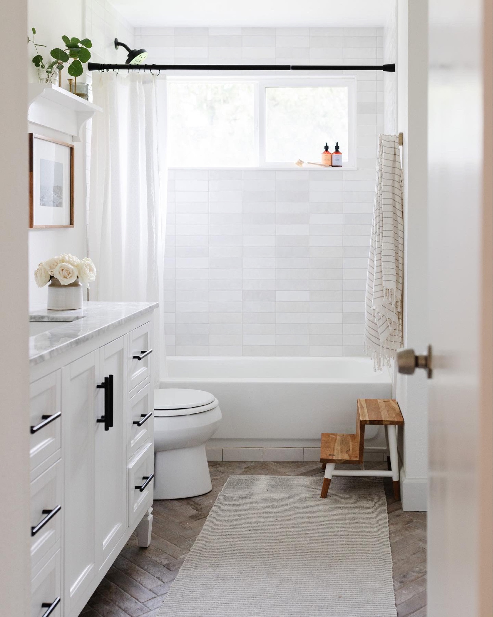 Simple white bathroom and white bathroom accessories. White vanity, teak step stool, herringbone floor tile, white shower curtain, black shower curtain rod 

#LTKunder100 #LTKFind #LTKhome