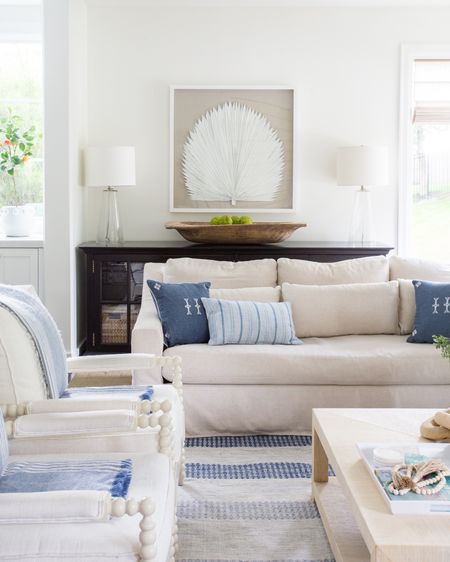 Items in our last coastal inspired living room include a blue linen pillow, a blue embroidered pillow, a slip covered sofa, white spindle chairs, blue and white throws and a blue and white striped rug. Other items include a raffia coffee table, a black sofa console, a wooden bowl, glass table lamps and a palm leaf art print. Items not shown include x-base stools, a woven seagrass basket, a wooden chain, a white vase with faux greenery, The Frame TV and a faux fiddle fig leaf tree. 

simple decor, family room, living room décor, Amazon finds, amazon home decor, serenaandlily rugs, pottery barn living room, rugs family room, family room decor, coffee table decor, pb inspired room, pottery barn décor, pottery barn furniture, pottery barn sofa, pottery barn throw, coastal decorating, coastal design, coastal inspiration, pottery barn dining room, pottery barn art, neutral decor, simple style, wall art, living room rugs, simple decorating #ltkfamily #ltkfind 

#LTKSeasonal #LTKstyletip #LTKunder50 #LTKunder100 #LTKhome #LTKstyletip #LTKsalealert #LTKhome