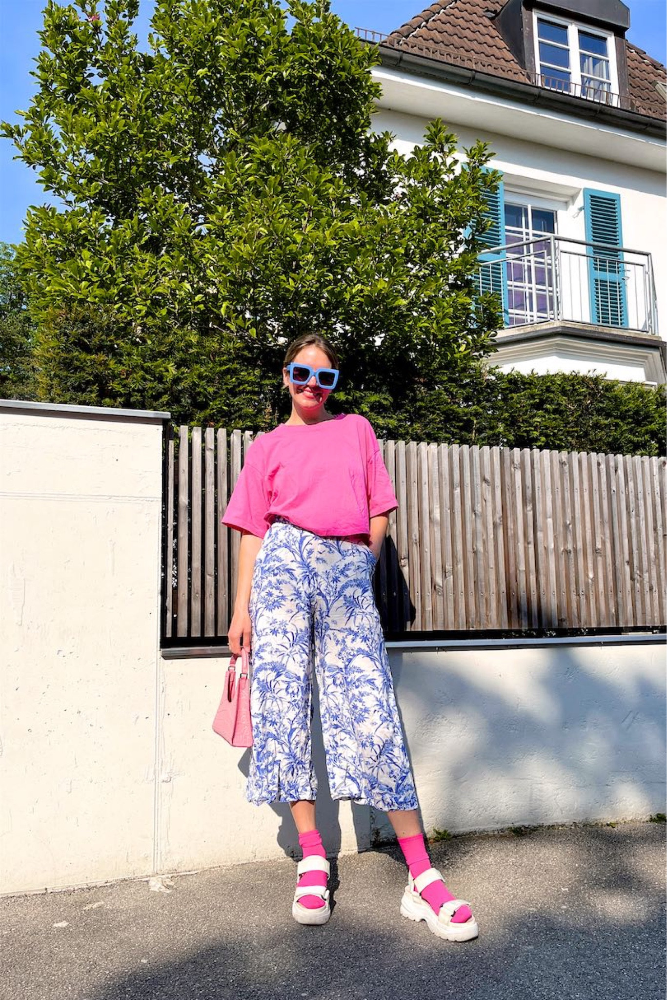Pink & Blue. Fashion Blogger Girl by Style Blog Heartfelt Hunt. Girl with blond sleek bun wearing a pink and blue color combination with a pink cropped T-shirt, blue printed summer pants, blue oversized sunglasses, pink Staud bag, pink socks and chunky sandals. #pinkandblue #summerpants #colorfuloutfit #colorfulstyle #colorfulfashion #colorfullooks #fashionfun #cutesummeroutfit #summerfashion2023 #summerlookbook #fitcheck #dailylooks #dailylookbook #contentcreator #microinfluencer #discoverunder20k 