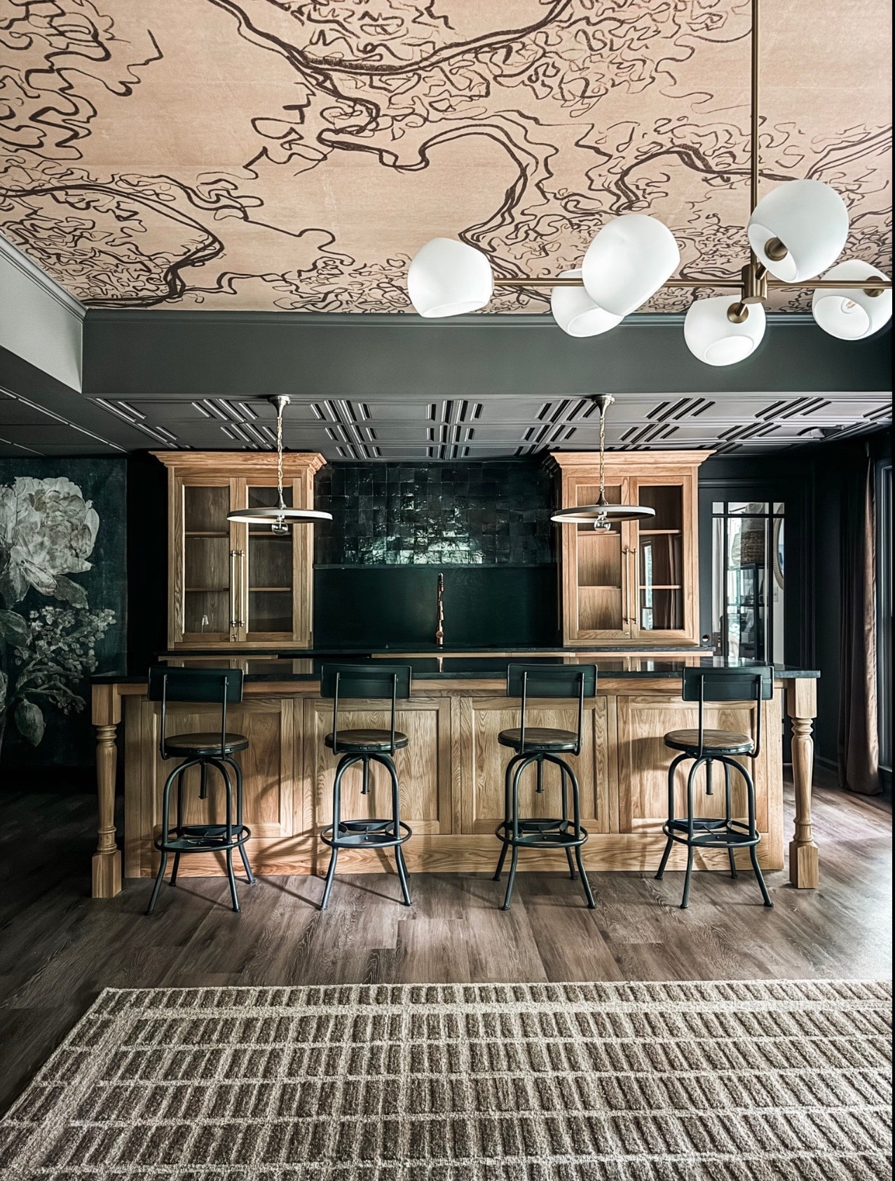 A moody home bar moment done right 🍸 This space layers custom wood cabinetry, a dark tile backsplash, and a statement coffered ceiling with patterned wallpaper for a rich, elevated look. The solid wood bar island, black metal bar stools, and brass pendant lighting bring warmth and contrast, while the modern chandelier adds a sculptural touch. Finished with wide plank wood floors and a neutral area rug, this bar feels both timeless and inviting—perfect for entertaining.

#eanesinteriors #homebar #homebardesign #barinspo #customcabinetry #woodcabinetry #barisland #barstools #brasslighting #pendantlighting #modernchandelier #cofferedceiling #wallpaperceiling #moodyinteriors #luxuryinteriors #ltkhomestyle #interiordesigninspo

#LTKOver40 #LTKHome #LTKSeasonal