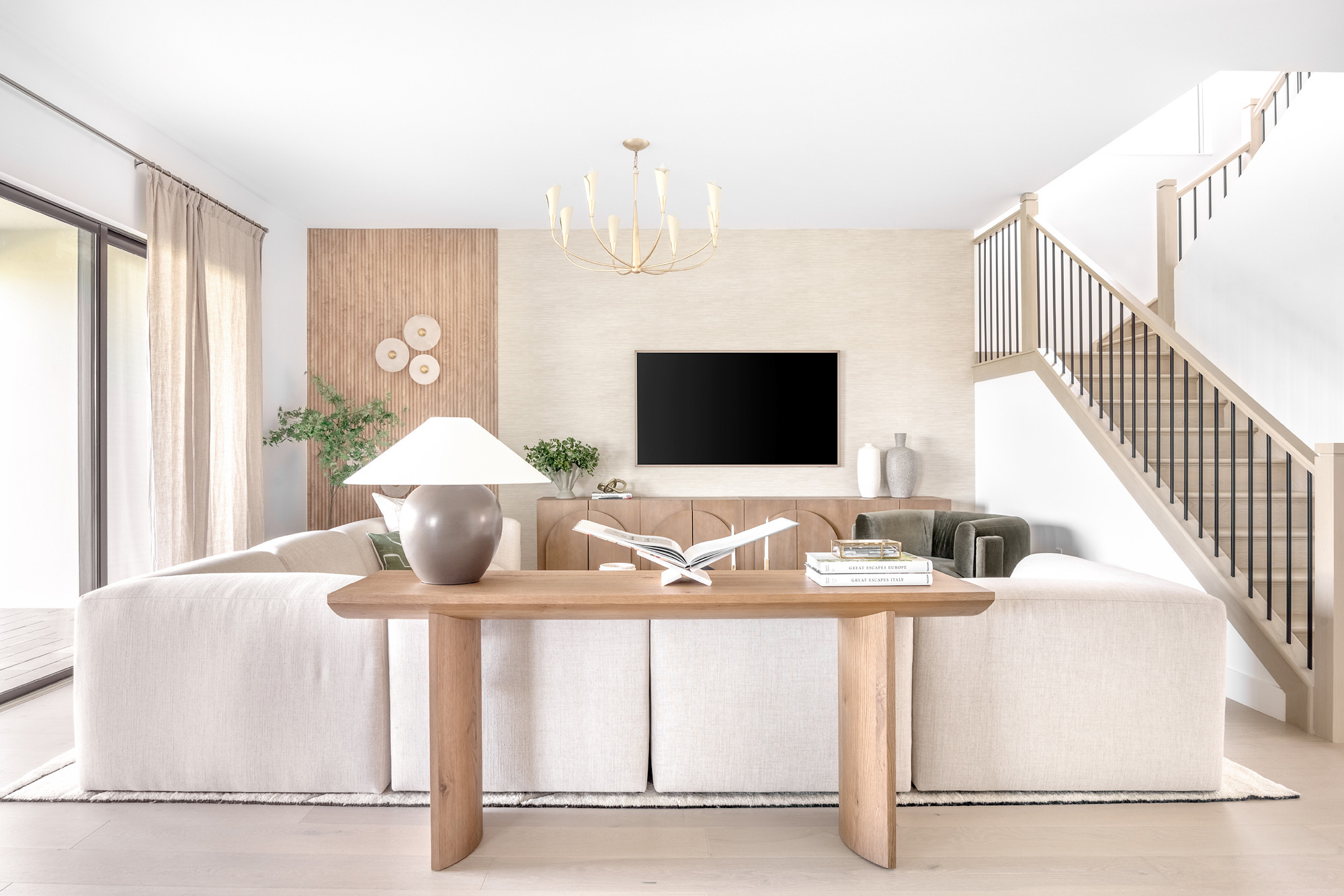 Introducing the Boca Raton Essex House by Studio 790 Interior Design living room. The lighting design elevates the room, from the brass chandelier's elegant glow to the wall-mounted fixtures that double as art. A textured area rug underfoot adds warmth and subtle detail, creating a cozy yet refined atmosphere. The backdrop features a beautifully crafted wooden credenza and curated decor, including books, ceramic vases, and natural greenery. This is a space where style meets functionality, ideal for both casual family moments and elevated entertaining. 

 #LTKHome