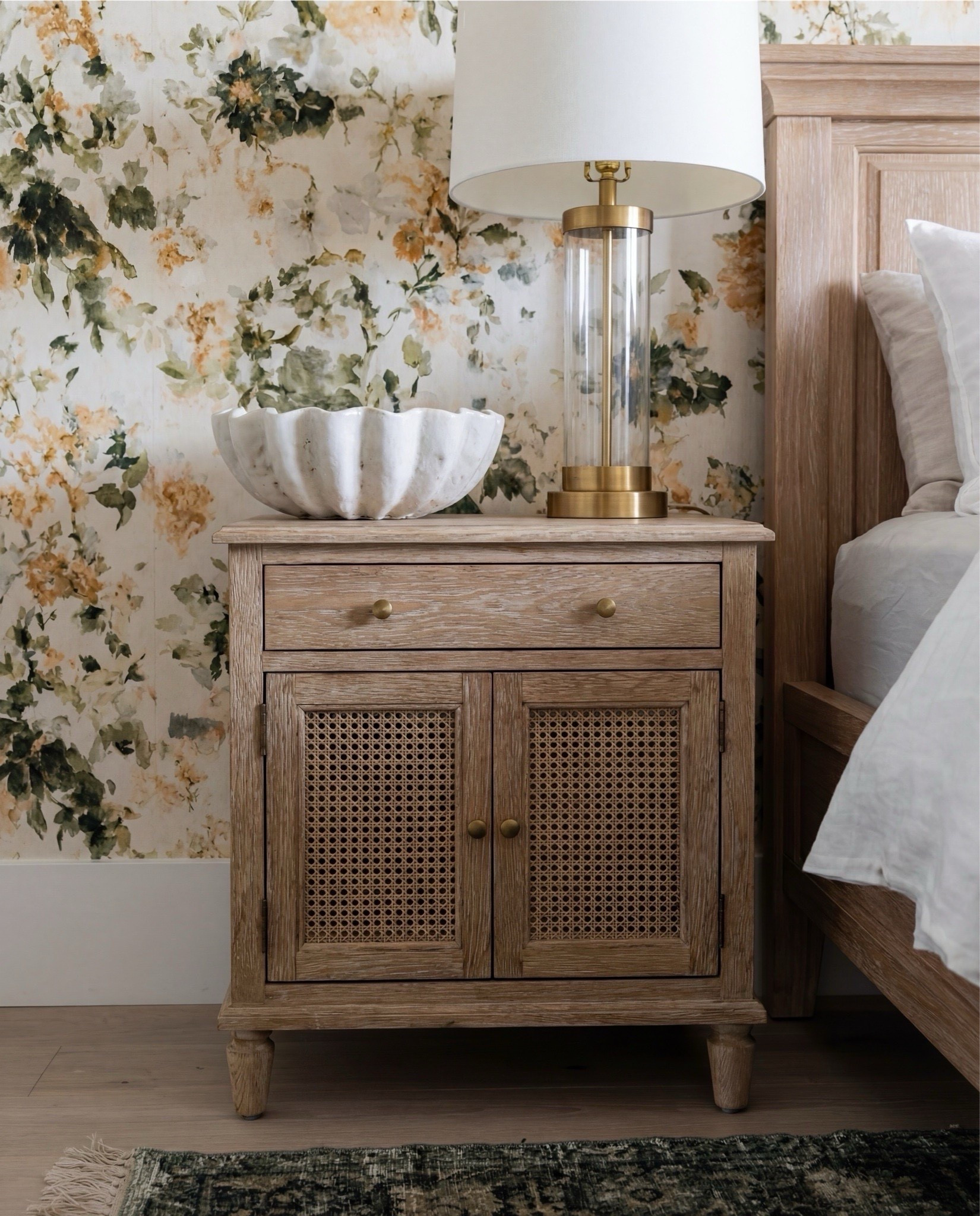 Shop the Look: Bedroom Refresh 
• Light oak panel bed
• Cream + green accent pillows
• Warm chunky knit throw
• Textured caramel cube ottomans
• Brass bedside lamps
• Fluted natural wood nightstands
• Green vintage-style rug
• Large white globe ceiling light
• Soft neutral pinch-pleat curtains
• Botanical floral wallpaper with soft gold + sage undertones

#LTKHome #LTKSaleAlert