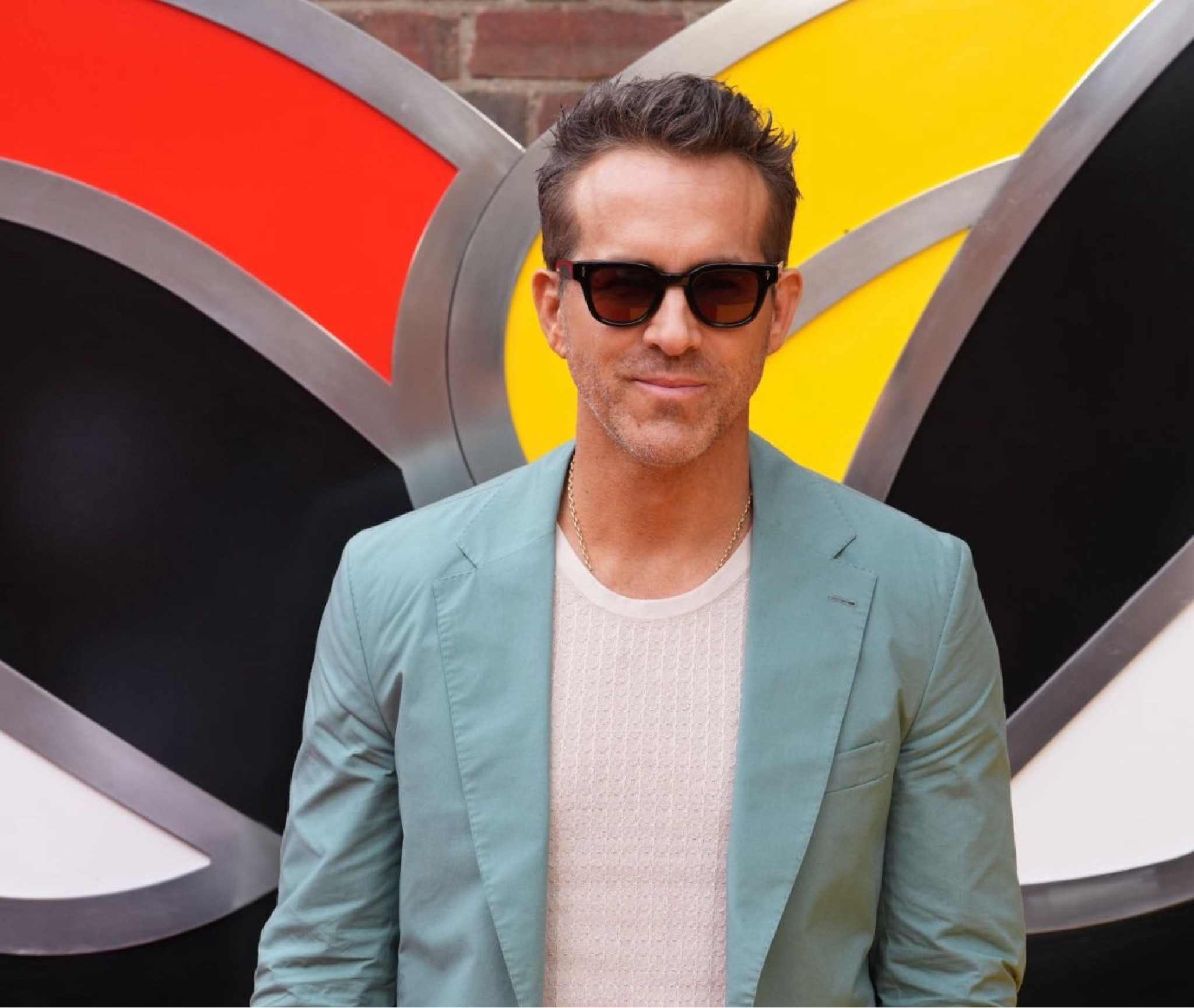 Ryan Reynolds in London promoting Deadpool & Wolverine wearing sunglasses with red lenses and a silk muscle tank top under his suit  