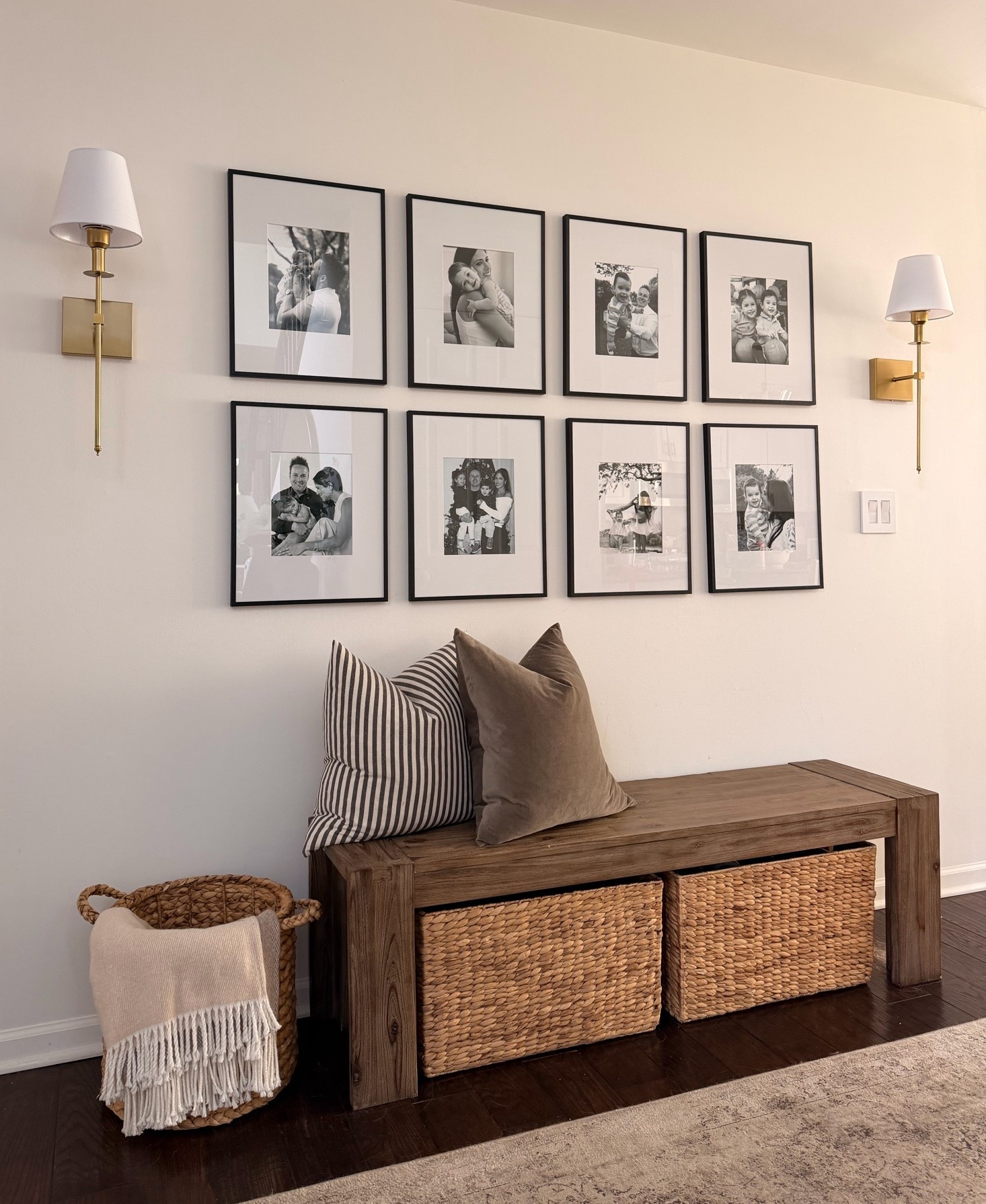 A little family gallery wall moment. Black frames, brass sconces, a wooden bench, and woven baskets to hide the shoes my kids leave everywhere. Warm, classic, and personal. Shop the look below.