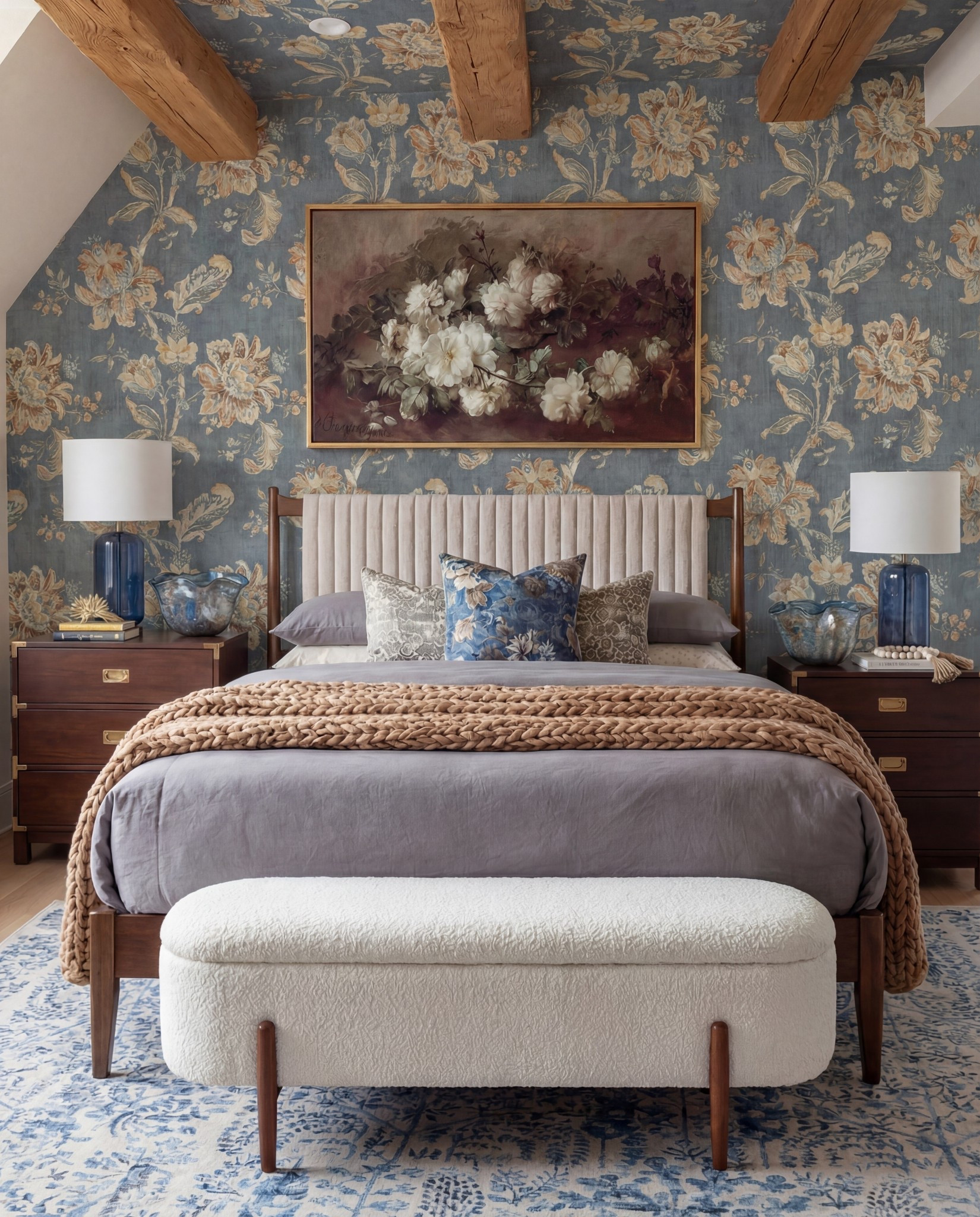 Shop The Look:
• Warm-wood platform bed frame
• Vertical-channel upholstered headboard
• Gray duvet cover + layered sheet set
• Mixed blue + neutral accent pillows
• Oversized chunky knit throw blanket
• Shearling-style upholstered storage bench at the foot of the bed
• Pair of dark-wood campaign-style nightstands with brass hardware
• White drum-shade table lamps with blue glass bases
• Blue decorative bowls
• Bead garland décor
• Stack of books (nightstand styling)
• Framed oversized floral artwork above the bed
• Blue floral wallpaper (full wall + ceiling)
• Exposed wood ceiling beams
• Blue patterned area rug
• Window bench with plaid/tan accent pillows

#LTKSaleAlert #LTKHome #LTKFindsUnder100