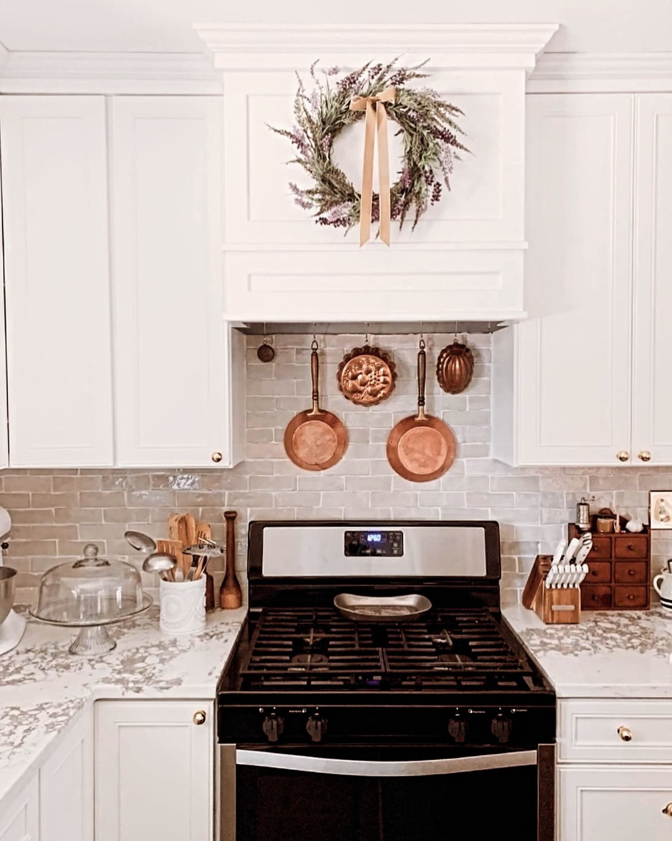 It seems designers are moving away from the sterile grey and white kitchen but white cabinets will continue to be a timeless classic. With the right finishes a white kitchen can be a warm and cozy place but finding the balance can be difficult. I have a few tried and true tips for bringing the warmth into a white kitchen. Our kitchen has white cabinets and walls but it’s one of the coziest rooms in our home and here’s why:

1. Copper- copper utensils, copper pans, and my absolute favorite- vintage copper jello molds. I love seeing them hanging behind the range.

2. Brass hardware- bonus points if they are unlaquered. The patina ours have developed over the last year and a half only adds to the warm, loved in feel.

3. Warm wood floors- the floor is one of the largest surfaces of the room and that shouldn’t be disregarded. We chose a warm, coffee brown and a lighter shade of brown for the kitchen island. I think a white island would have felt cold, especially with the countertops I chose which are white and gray with a brown veining.

4. Wicker- every room should have some variation of wicker, even the kitchen. Baskets are versatile and add texture which helps cozy a space up.

#englishcottage #cottage #acnhcottagecoreinspo #cottagecoreaesthetic #cottagekitchen #frenchcountrystyle #frenchcountry #frenchcountryside #frenchcountrydecor #kitchen #kitchendesignideas #kitchendesign #kitchensofinstagram #ａｅｓｔｈｅｔｉｃ