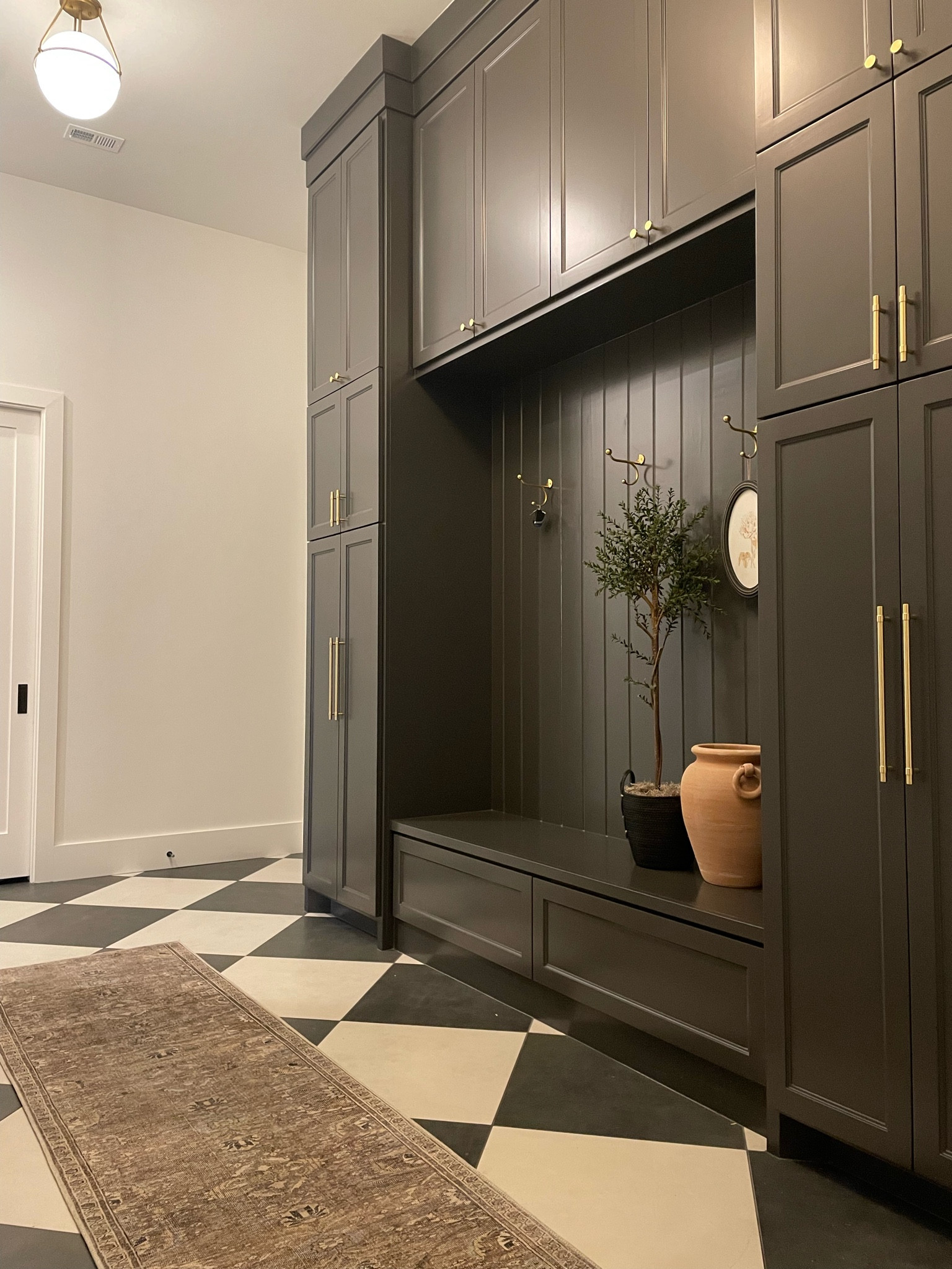 Mudroom styling, runner, washable rug, olive tree, brass hardware, Sherwin Williams Iron Ore, checker floors, modern home, mudroom, utility room. 

#presidentsdaysale #ltkhome #ltksale #kellerandoak #washablerugs #rejuvenation 