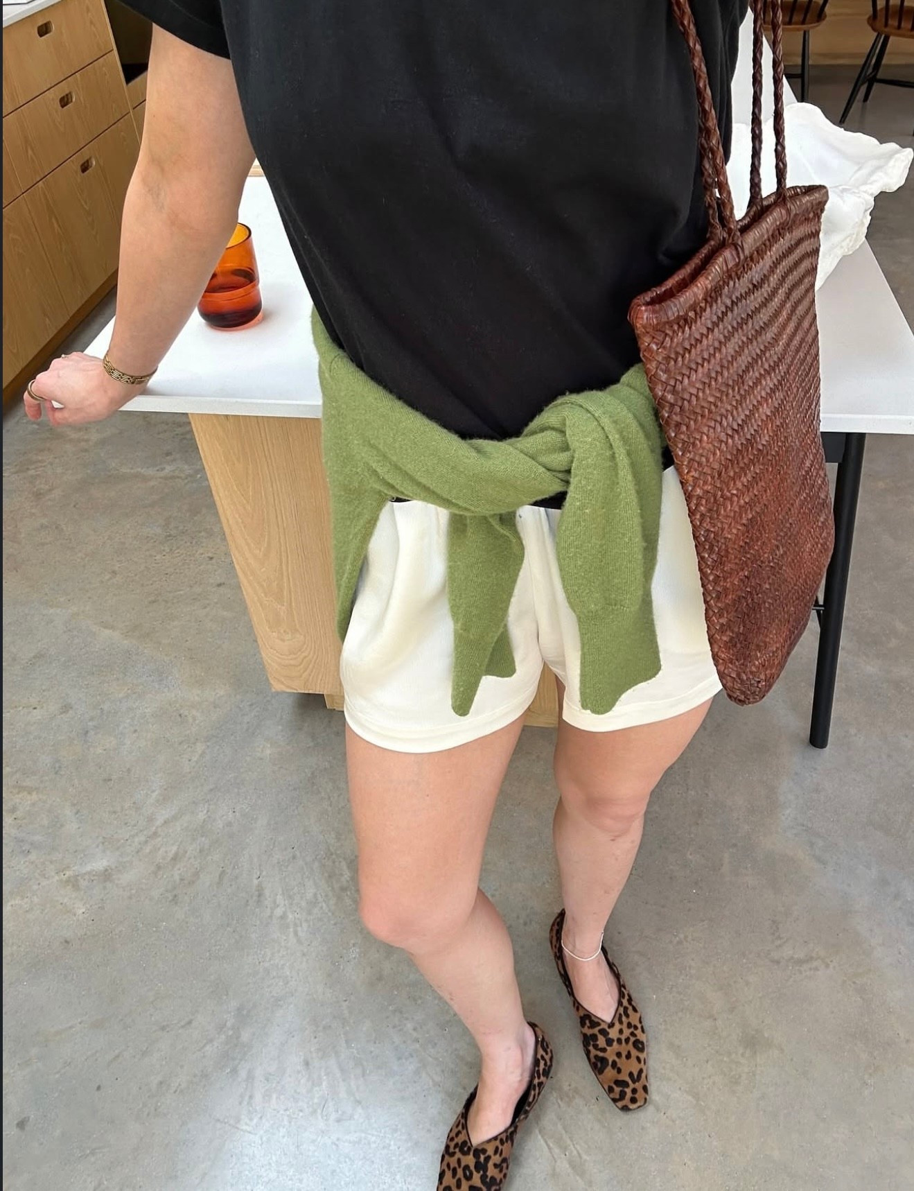 A simple base of a black tee and cream shorts, elevated with a pop of colour from the green knit, animal print flats, and a woven tote for added texture. Perfect for everyday plans, coffee runs, or travel days.