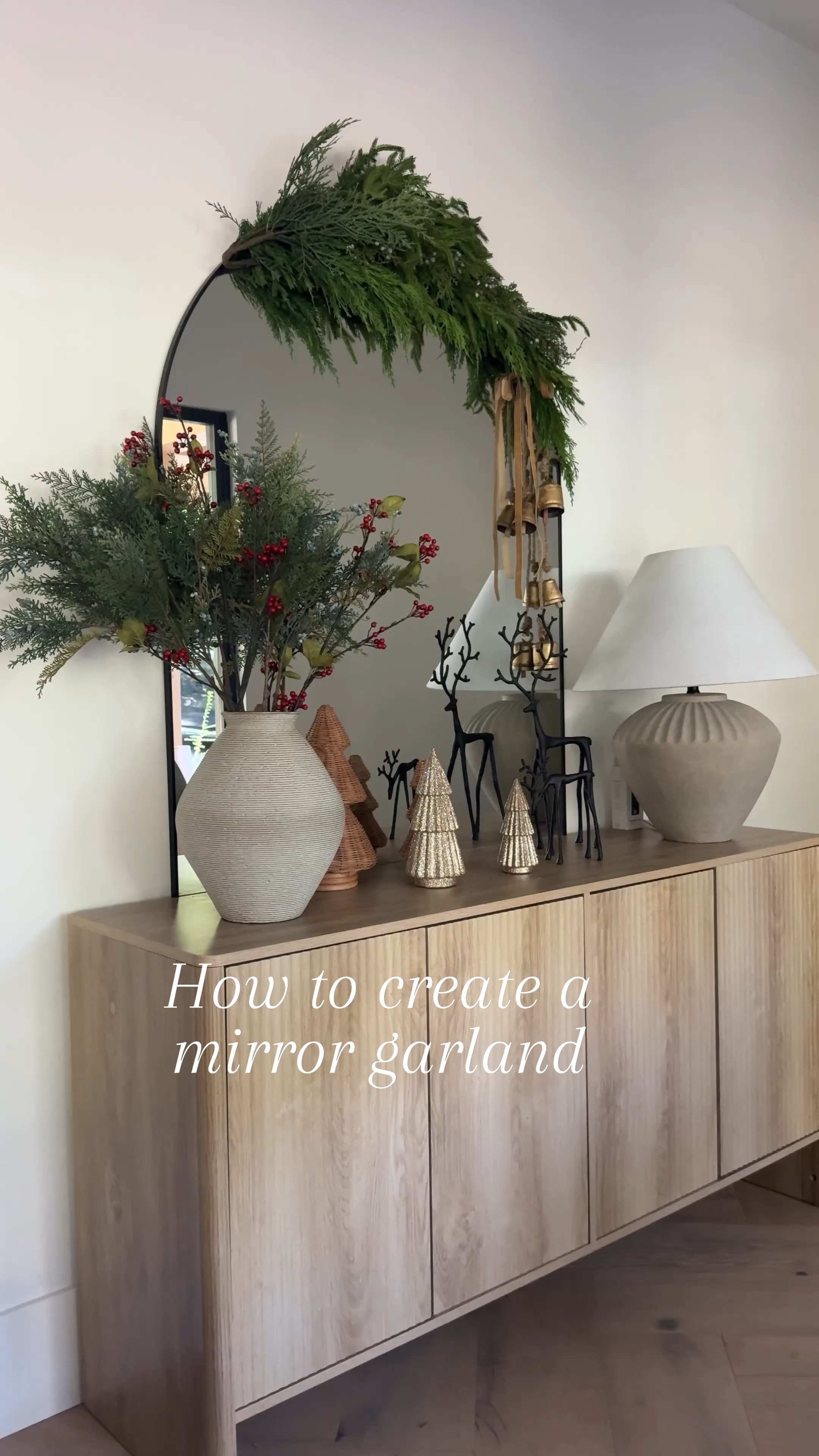 How to style a mirror garland. Love this new addition to our entryway. Gray table, lamp, black reindeer, glitter trees, rattan trees, Christmas trees, Holly Spriggs, grave, vase, wood sideboard, wood console, table, brass bells, green garland, floor, mirror, black arched, mirror. Walmart, Wayfair Amazon. Gold ribbon vintage bells. Target

#LTKFindsUnder100 #LTKHome #LTKSaleAlert