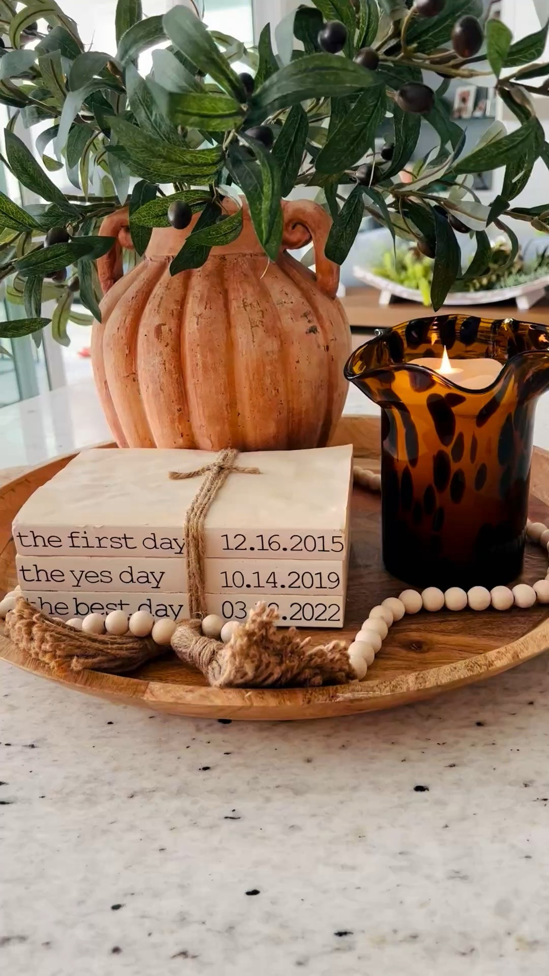 Little corners of home tell the story best 🤍✨
A few of my favorite things layered together on the kitchen counter… faux olive branches in a ceramic pot, the warm glow of a tortoise shell candle, and one of my most meaningful pieces — stacked “books” with the dates that changed our lives forever: when we met, got engaged, and got married. Finished with wood beads and tassels for that collected coastal touch.

It’s amazing how décor can hold memories too. 🤎

#LTKHome #CoastalHome #KitchenStyling #CountertopStyling #NancyMeyersStyle #CoastalLiving #NeutralHomeDecor #HomeDetails #EverydayElegance #AnchorGirlLiving