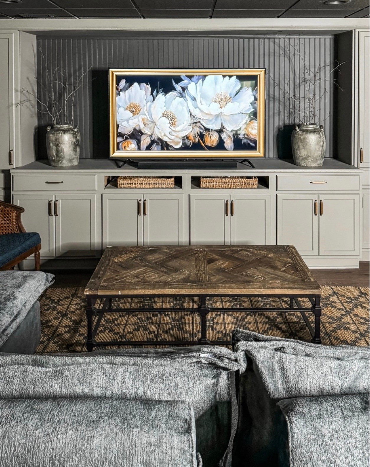 A timeless living room moment 🤍 This space is anchored by custom built-in cabinetry, soft gray cabinets, and a vertical shiplap accent wall that adds texture and depth. The large floral artwork with gold frame becomes the focal point, styled with ceramic vases, decorative branches, and woven storage baskets. Finished with a rustic wood coffee table, neutral area rug, and cozy upholstered sofa, this setup blends classic home decor with a modern farmhouse feel—perfect for a warm, elevated family room.

#eanesinteriors #livingroomdecor #builtinhelves #builtinmedia #customcabinetry #neutraldecor #modernfarmhouse #coffeetable #woodcoffeetable #arearug #wovenbaskets #homedecor #interiordesign #ltkhome #ltkdecor

#LTKHome #LTKOver40 #LTKSeasonal