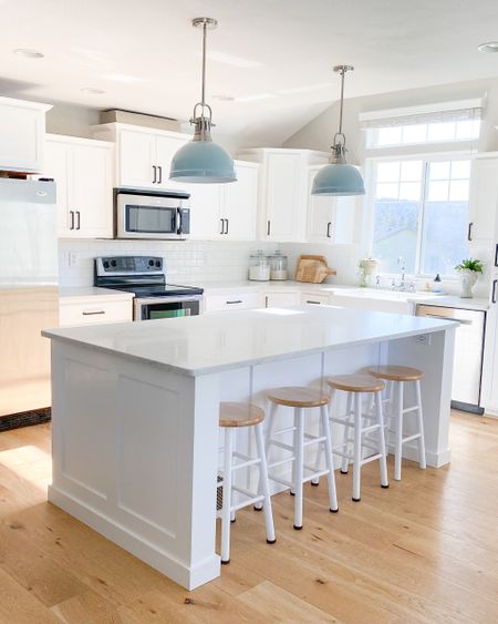 Light filled kitchen. Farmhouse white kitchen. Classic kitchen. Blue pendant light. Island Lightning. Barstools. Wood cutting board. Glass flour and sugar containers. Bust of Greek womanplant pot. Deep white kitchen sink. Bamboo dish scrubber  