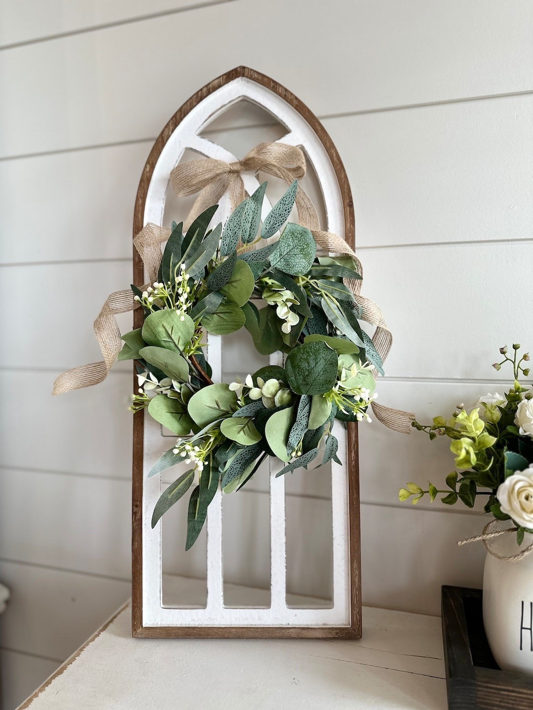 Add a touch of timeless elegance to your space with this whitewash cathedral window wall decor by CountryHomeandHeart. Featuring a beautifully arched wood frame, soft eucalyptus wreath with berries, and a charming burlap bow, this piece blends rustic warmth with classic design. Perfect for styling beside artwork, above nightstands, or in an entryway, it brings a cozy, elevated feel to any room with minimal effort. #LTKHome #FarmhouseDecor #WallDecor #RusticElegance #NeutralHome #CozySpaces #HomeStyling #TimelessDecor

#LTKSeasonal #LTKWedding #LTKHome