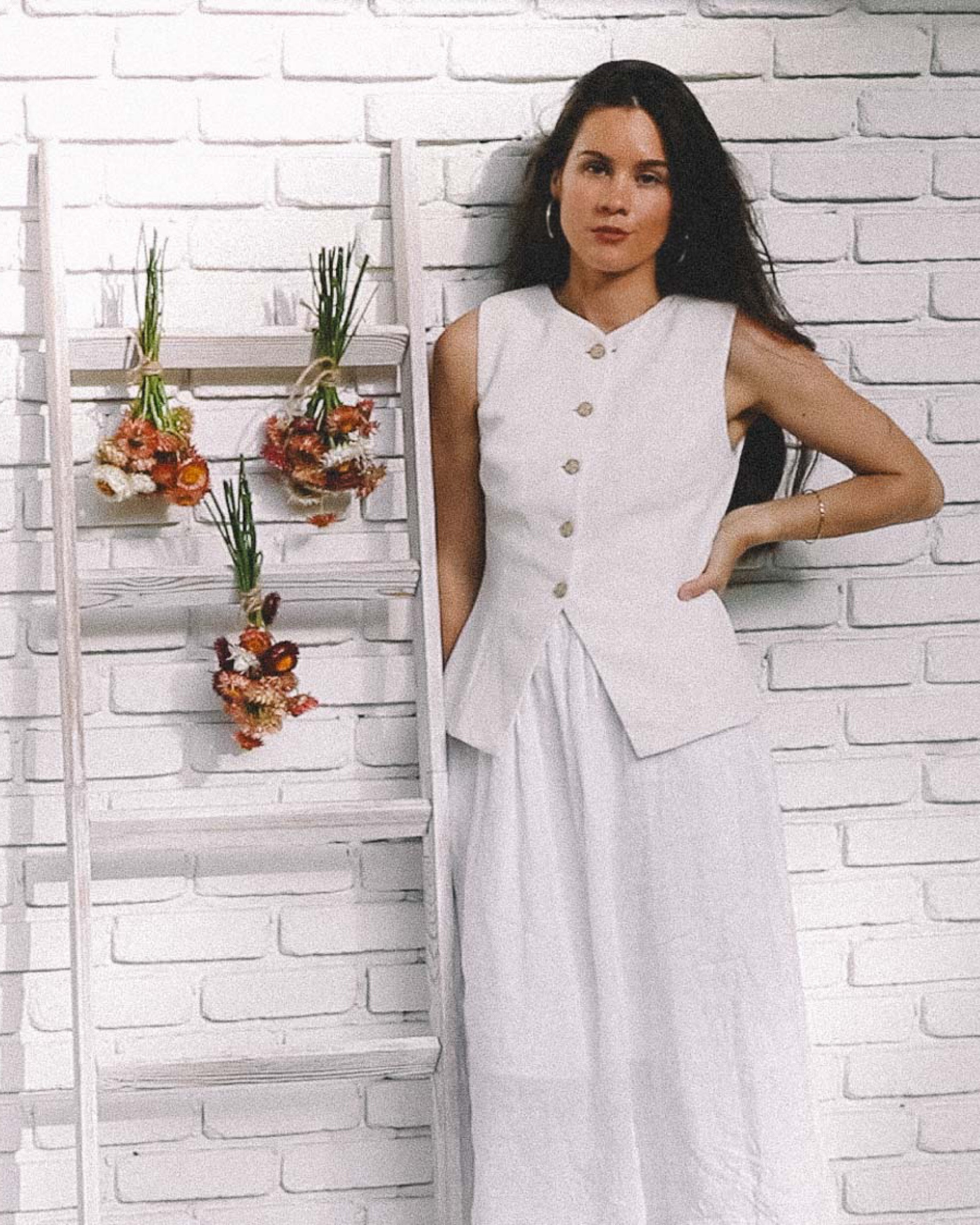 Minimalist White Outfit with Strawflower Decor for a Chic, Natural Look. Sarah dressed in a sleeveless white buttoned vest top and matching flowing white  linen skirt stands next to a simple wooden ladder adorned with bundles of dried strawflowers. minimalist fashion, white outfit, strawflower decor, natural aesthetic, dried flowers, eco-friendly fashion, boho style, rustic floral arrangement, simple chic style, nature-inspired decor, sustainable fashion

#LTKSeasonal #LTKFallSale #LTKHome