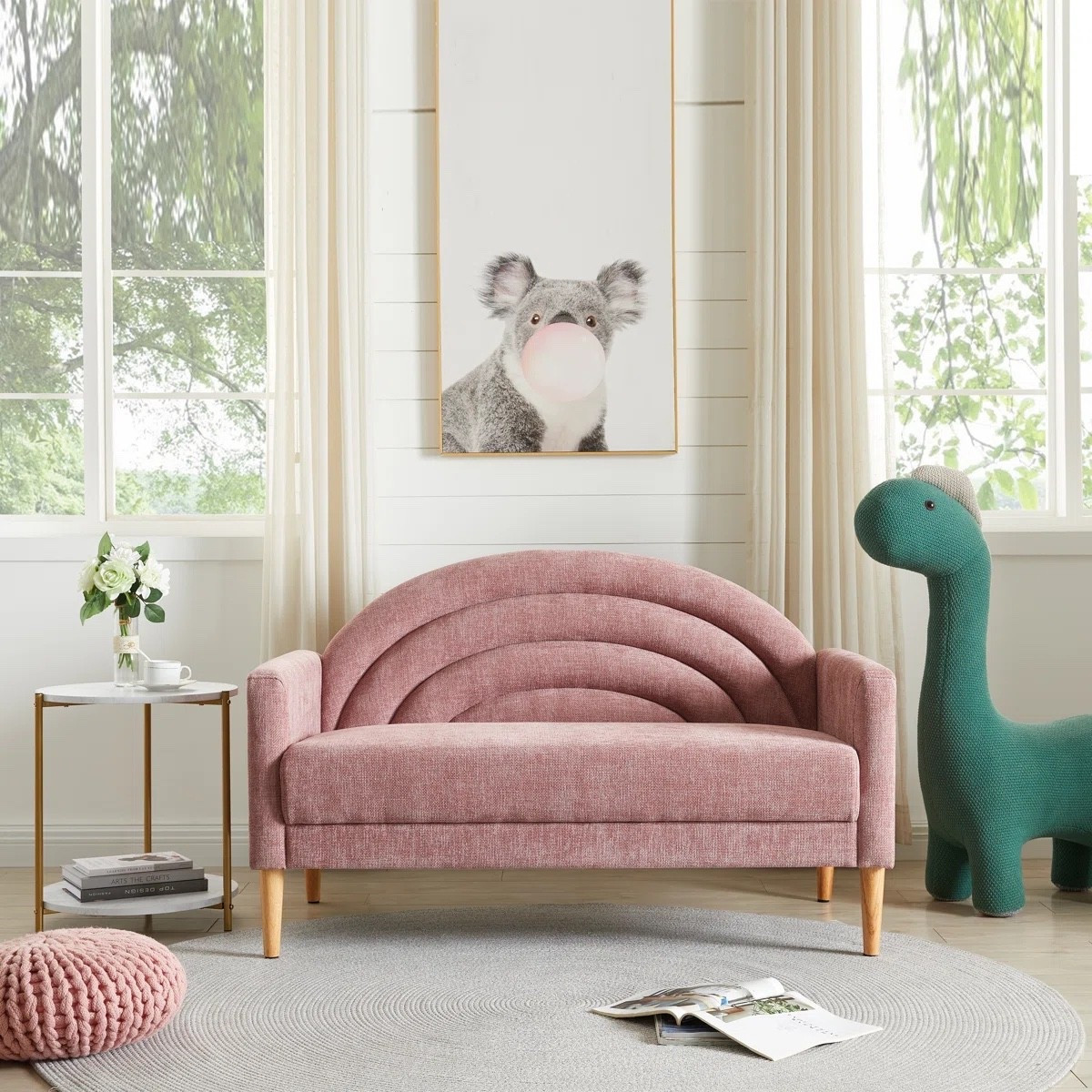 This pink upholstered loveseat from Wayfair is such a sweet statement piece for a living room, nursery, or kids space. The soft blush fabric, curved rainbow style back, and tapered wood legs make it both playful and modern. Style it with a round area rug, side table, and wall art for a cozy, styled corner.