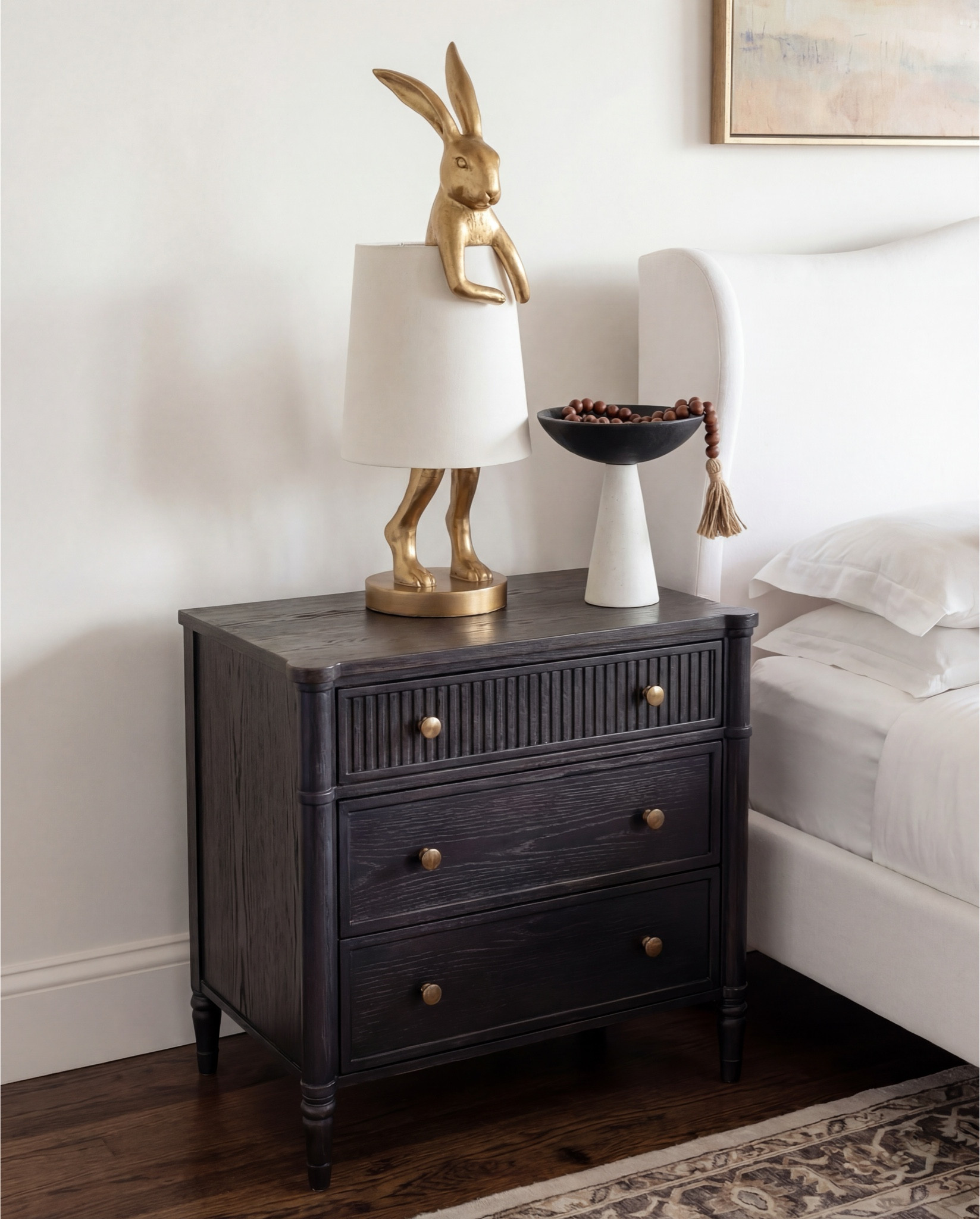 Shop the Look:
• Upholstered wingback bed (ivory fabric)
• White cotton bedding set
• Neutral euro pillows
• Black and tan patterned accent pillows
• Chunky knit throw blanket (camel brown)
• Dark black wood nightstands
• Decorative bunny Brass table lamps with white shades
• Framed abstract wall art (neutral tones)
• Vintage-style area rug (beige and taupe)
• Dark black wood dresser with brass hardware
• Brass ring drawer pulls
• Glass hurricane candle holders
• White pillar candles
• Decorative brass tray
• Sculptural brass decor object
• Small stone sculpture 
• Light beige linen curtains
• Ceramic vase (off-white)
• Decorative branches
• Coffee table books (neutral covers)
• Upholstered bench at foot of bed (cream fabric)
•upholstered wood accent chair 
•round ribbed black end table 

#LTKSaleAlert #LTKFindsUnder100 #LTKHome