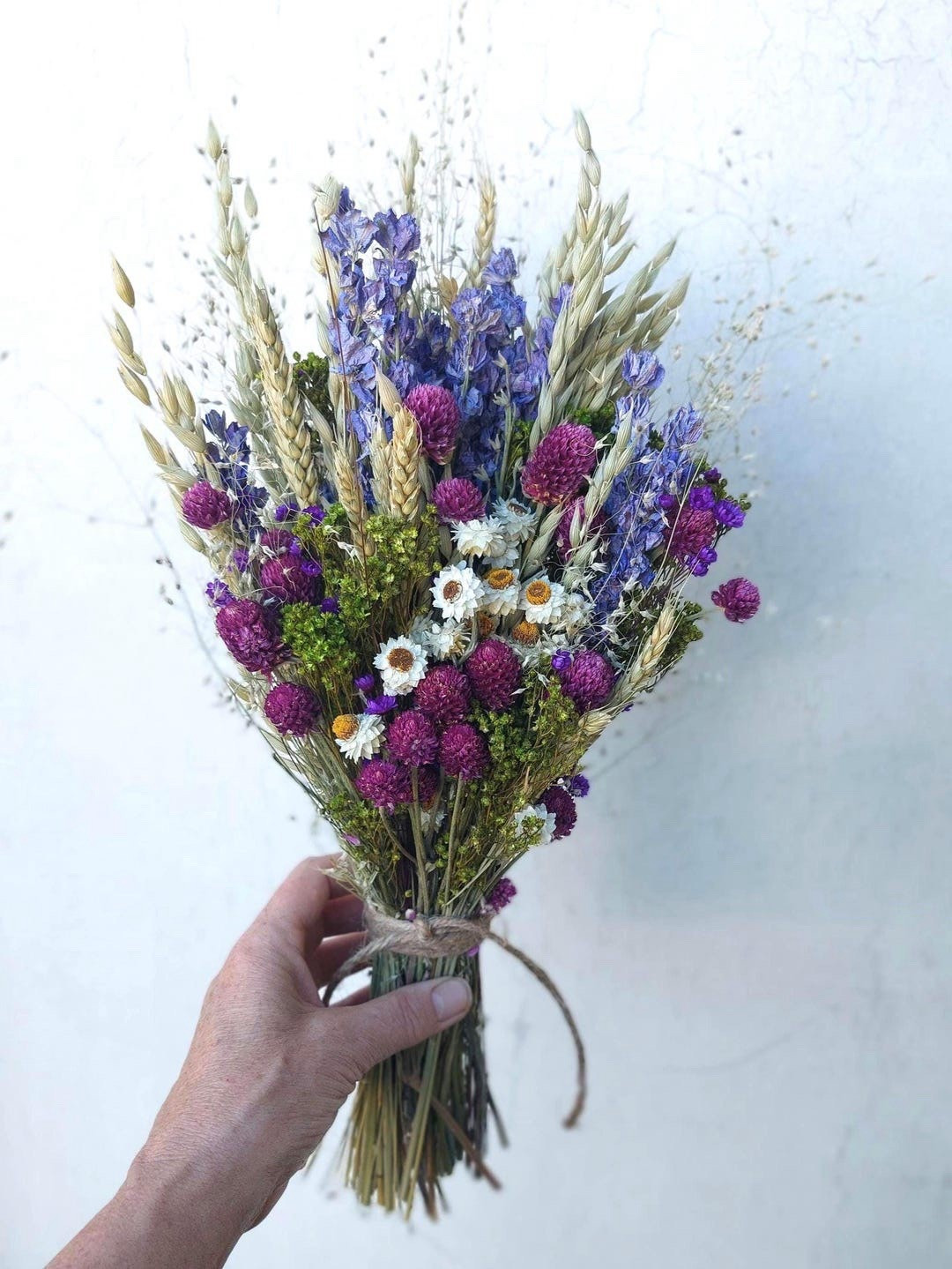 Bring the beauty of a spring meadow indoors with this handcrafted dried flower bouquet in soft shades of purple and natural textures. Featuring gomphrena, lilac wildflowers, ammobium daisies, and airy grasses, this flat-backed bouquet is perfect for styling on a mantel, shelf, or in your favorite vase. Finished with natural jute twine, this arrangement offers effortless, long-lasting charm and a touch of nature-inspired elegance for any space.

#LTKHome #LTKFinds #DriedFlowers #FarmhouseDecor #HomeDecor #PurpleDecor #FloralDecor #EverlastingFlowers #RusticDecor #SpringDecor #ShelfDecor #MantelDecor #NaturalDecor #HomeInspiration #MeadowStyle

#LTKHome #LTKWedding #LTKSeasonal
