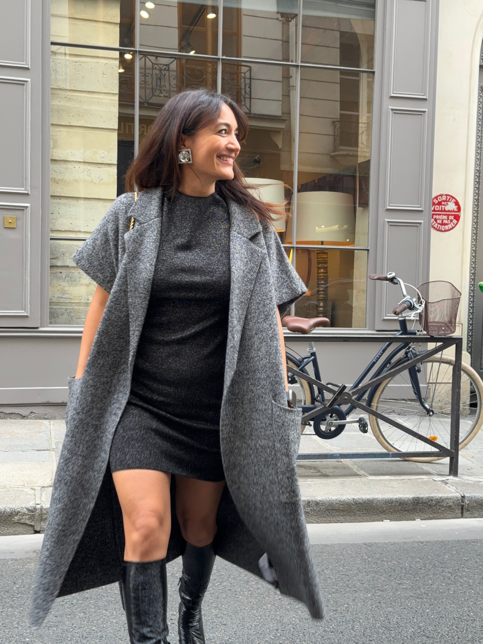 Look avec un manteau gris sans manches cosy pour ce début d’automne. Porté avec une petite robe simple et des bottes vernies noires 