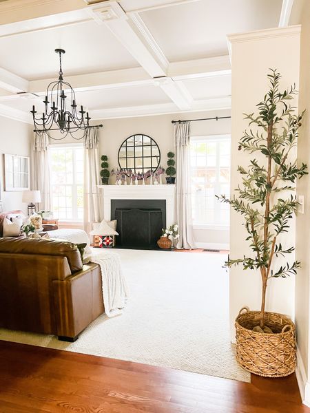 Summer family room. Neutral decor. Olive tree. Milk glass vases with mini flags. Iron chandelier. Large round black mirror. Drop cloth curtains.

#LTKFind #LTKhome #LTKstyletip