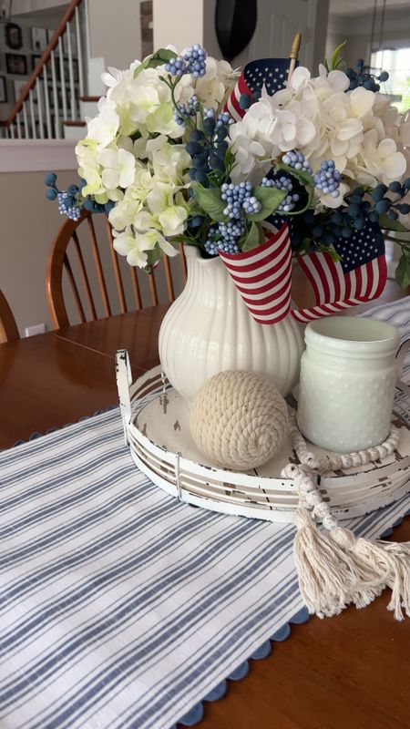 Summer tablescape. Simple summer centerpiece. White pitcher. Faux white hydrangeas. Faux blueberry stems. Mini American flags. Rope orb. Blue and white striped table runner.

#LTKhome #LTKstyletip #LTKSeasonal