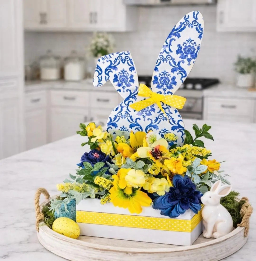 Brighten your spring decor with this charming blue, yellow, and white Easter centerpiece featuring a beautiful chinoiserie-style bunny. Designed in a white wooden box and accented with cheerful yellow blooms, navy florals, and soft greenery, this arrangement brings a fresh designer look to your home. Perfect for an Easter table, coffee table, kitchen island, or entryway display, this handcrafted piece adds a cheerful pop of color and elegant seasonal charm to any space. 🌼🐰

#LTKHome #LTKSpring #EasterDecor #ChinoiserieDecor #SpringCenterpiece #EasterTable #BlueAndWhiteDecor #SeasonalDecor #HomeStyling #SpringHome

#LTKSeasonal #LTKHome #LTKSpringSale