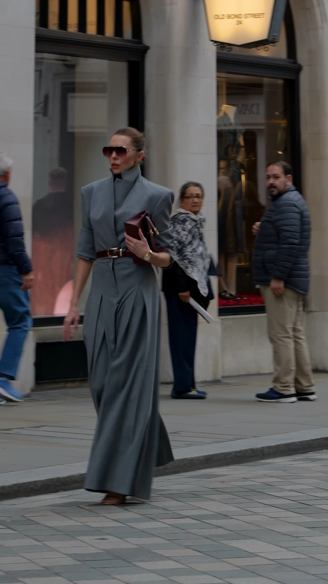 This look features a structured grey suit from ASOS, consisting of a sharp, high-collared blazer and matching wide-leg tailored trousers. The blazer has strong shoulders and a cinched waist, creating a sculpted silhouette, while the pleated trousers add volume and movement. Styled with a burgundy belt and matching handbag, oversized sunglasses, and understated gold jewelry, the look channels sleek, modern power dressing with a refined, fashion-forward edge.

#LTKautumn #LTKeurope #LTKuk