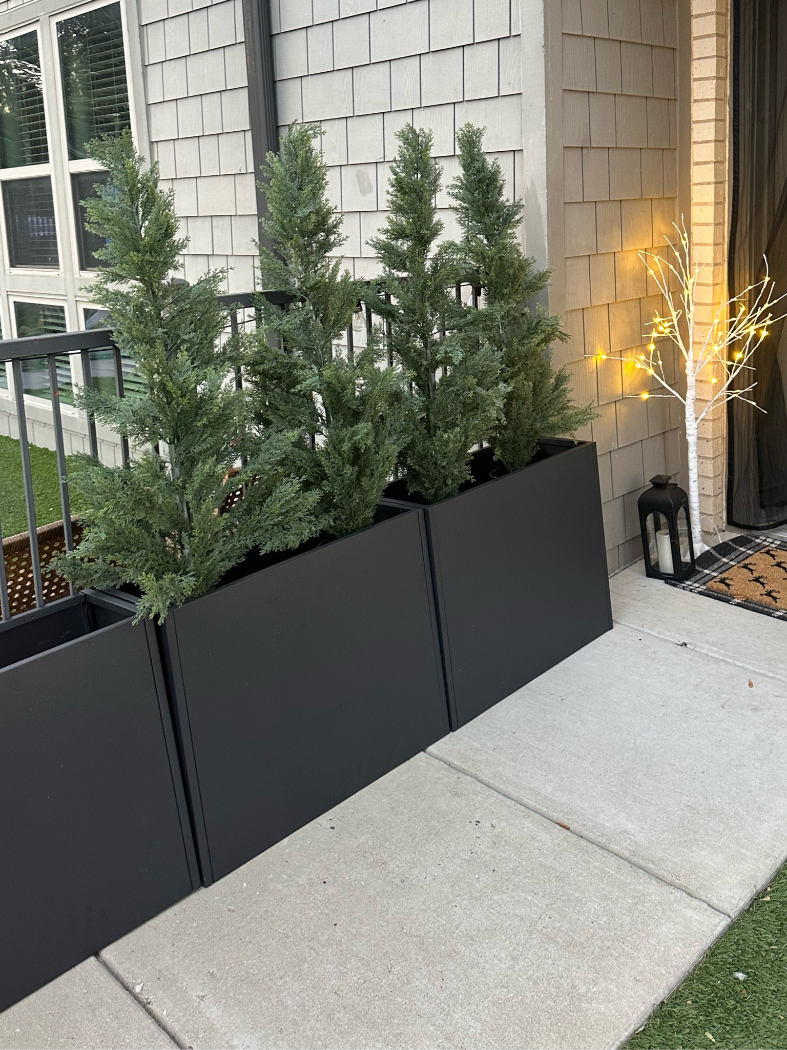 Artificial cedar trees and black metal weatherproof planter boxes for an outdoor privacy wall! 