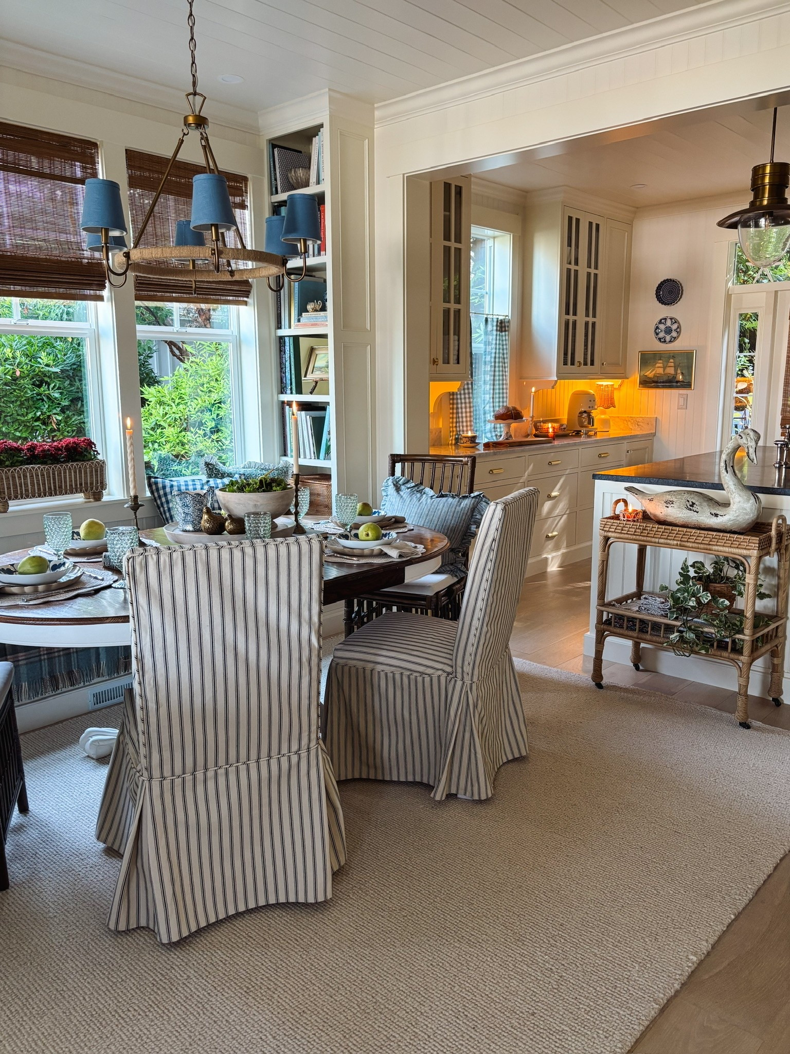 Coastal cottage dining room and kitchen - Slipcovered chairs, rattan cart, chandelier with shades, bamboo shades, gingham cafe curtains