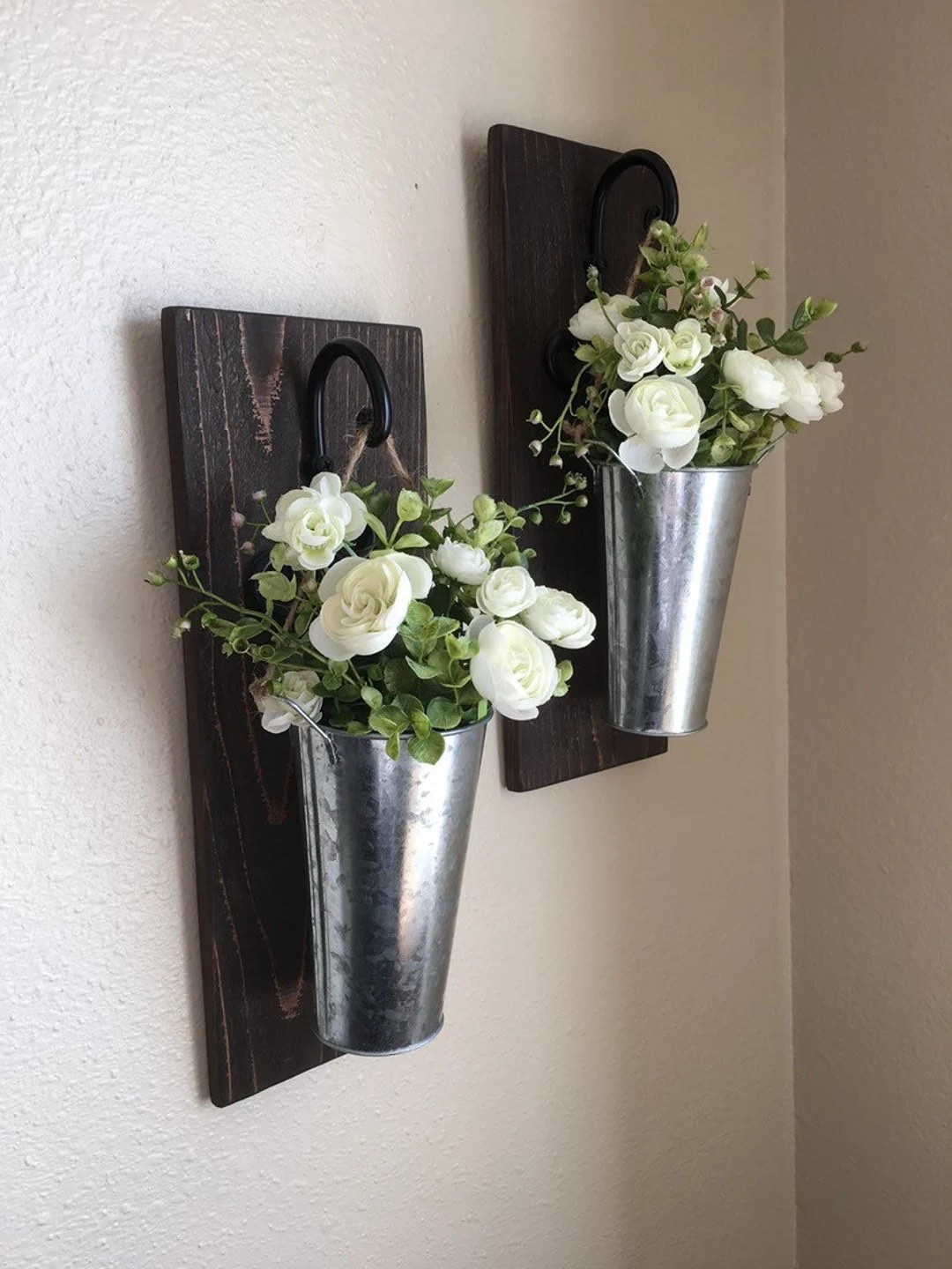 Add a touch of farmhouse charm to your walls with these hanging galvanized vase sconces, designed to bring texture and greenery into your space. Featuring a blend of hydrangeas and boxwood tucked into rustic metal buckets on a wooden base, each set can be customized to fit your style—from full florals to simple greenery or even a minimalist look. Perfect for creating a cozy, layered wall display in any room. #LTKhome #farmhousedecor #walldecor #rusticstyle #greenerydecor #homestyling #cozyhome #decorinspo

#LTKSeasonal #LTKWedding #LTKHome