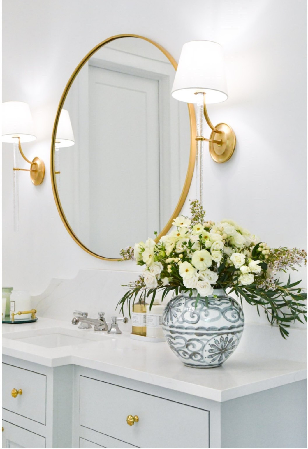 Primary bathroom home decor
Round gold mirror 
Gold wall sconces, lighting
Faucet
Gold tray
Blue and white vase 

#LTKHome