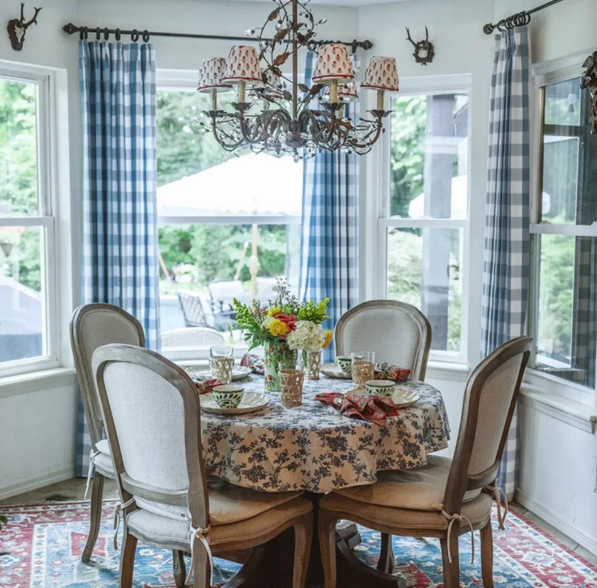 Custom pinch pleat blue buffalo check curtain panels. Buffalo check drapes, crystal chandelier, pleated chandelier lampshades, rug, upholstered linen wood dining chairs, blue floral tablecloth 

#LTKHome #LTKSeasonal #LTKSaleAlert
