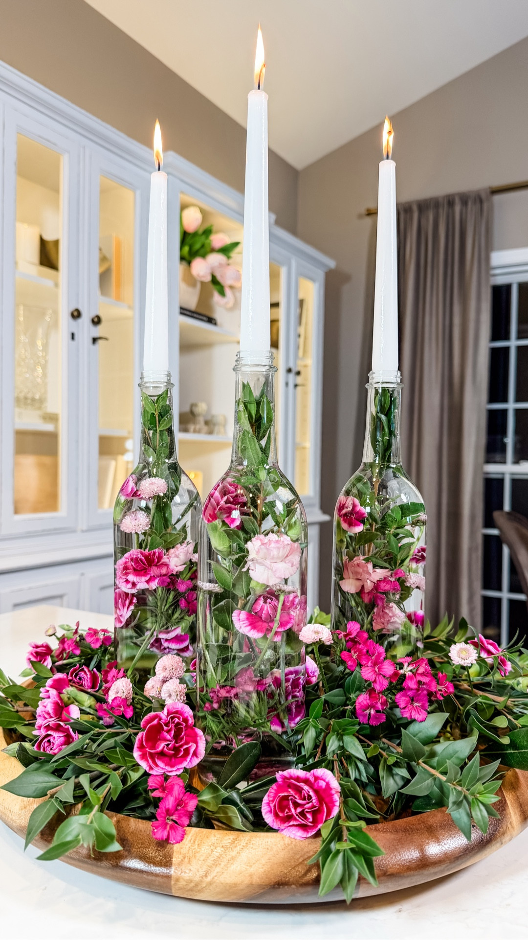 Floral Candlelight Centerpiece ✨🌸An easy centerpiece idea I love for spring and summer. Simple glass bottles filled with florals and topped with taper candles create height, glow, and that effortless “looks like a florist did it” feel.

Styled on a wooden tray with extra blooms and greenery tucked around the base for a lush, garden-gathered look. It’s beautiful as a centerpiece or placed down the length of a table for a layered, romantic tablescape.

Perfect for Easter, garden parties, or summer dinners with friends. 🌿🕯️

#LTKSeasonal #LTKspring #LTKHome