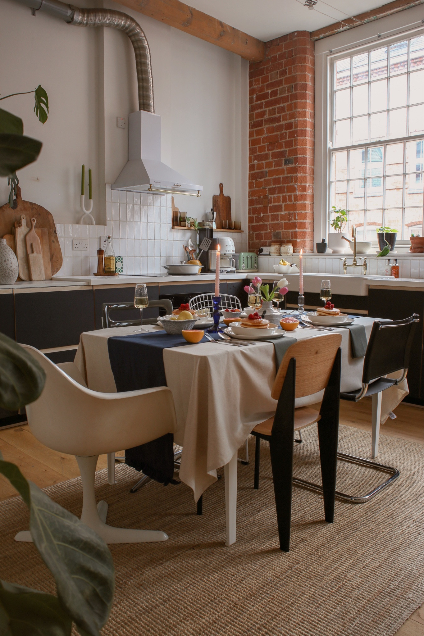 Black industrial factory apartment kitchen with high ceilings large old windows and eclectic mismatched dining chairs. Jute rug, white rectangle tile and white extractor fan. Exposed brick

#LTKeurope #LTKhome #LTKMostLoved