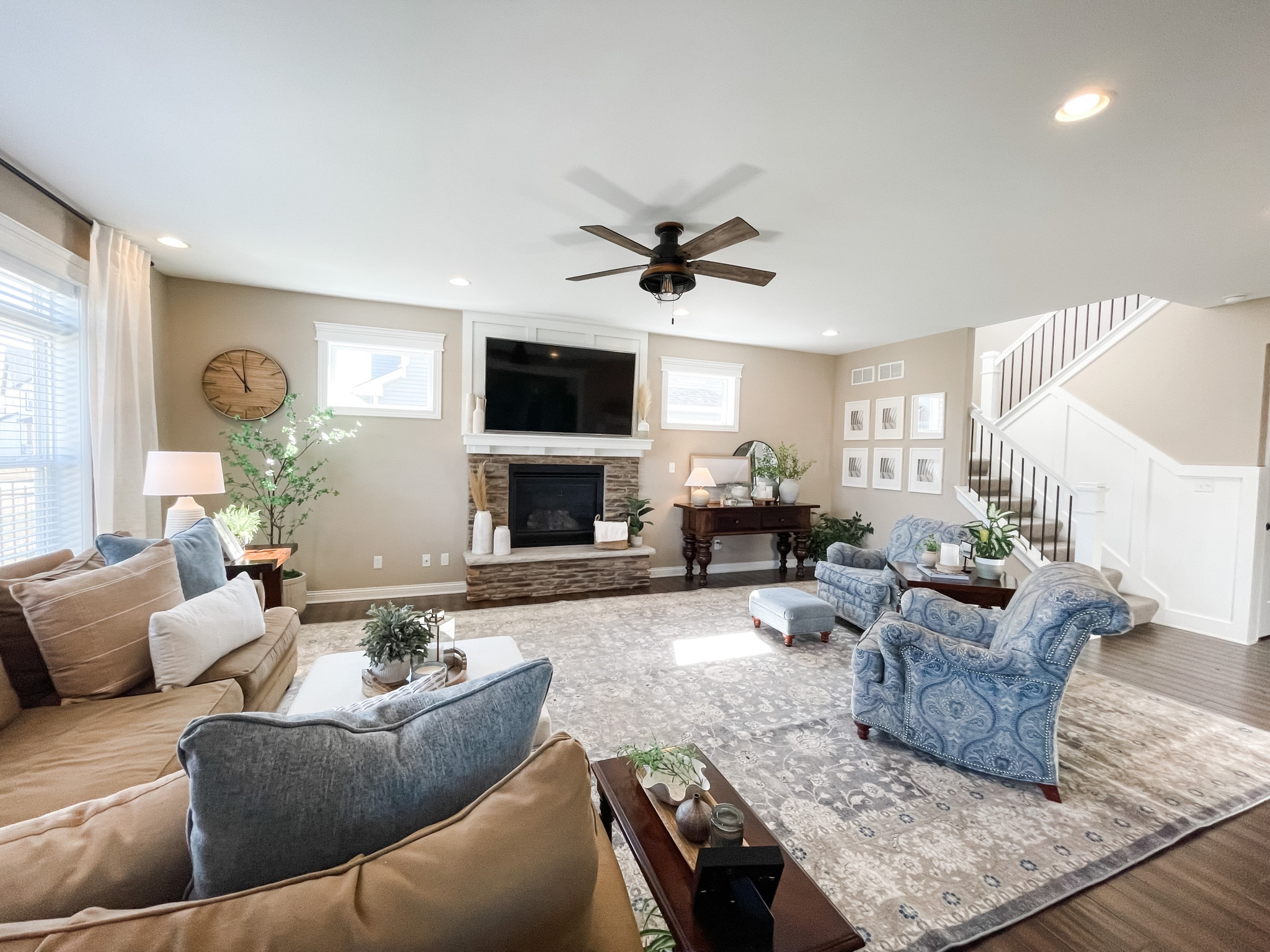 This is a living room with rug, couch, blue chair, lamp, round mirror, potted plant, fireplace, pampas grass, wood clock, wall art, pillows, tray, pot, table decor, blanket, basket, candle, ottoman, and picture frame.

#LTKhome