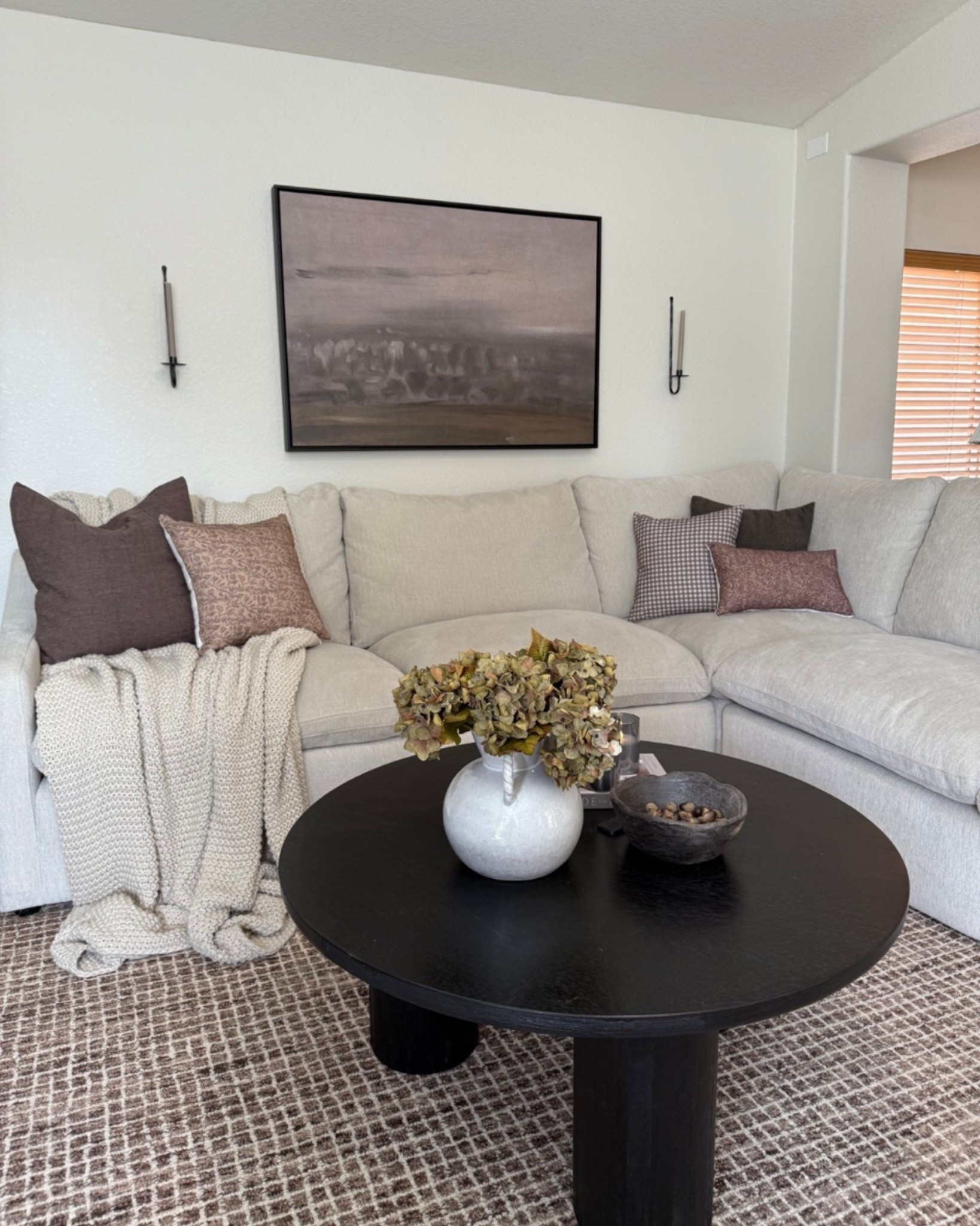 Living room views 😍 2 years later and we are still in love with our sectional! It’s so incredibly comfortable and I love that we have recliners too. 
•
•
•
Neutral living room, light sectional, light grey sectional, light grey couch, round coffee table, black coffee table, abstract wall art, framed canvas art, moody art, cove prints, candle sconces, candle wall sconce, brown rug, brown checked rug, pillow combos for couch, throw pillows for sectional

#LTKHome #LTKSeasonal #LTKSaleAlert