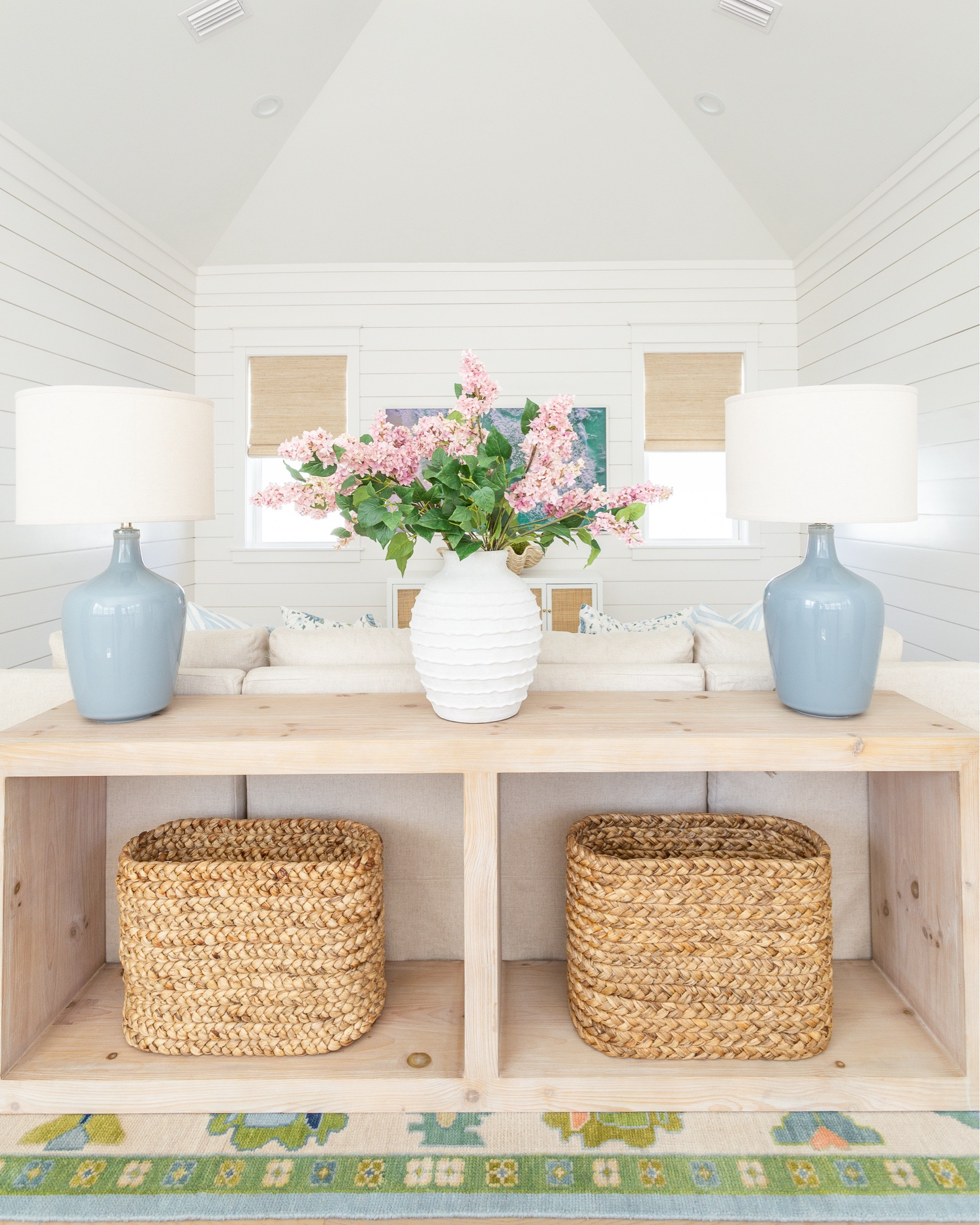 A peek at our loft living room decorated for spring! I used these pink lilac stems, ribbed white vase, colorful oushak rug, linen sectional, light wood console table, blue lamps, woven Roman shades, cane media cabinet and Frame TV in this room.
.
#ltkhome #ltksalealert #ltkfindsunder50 #ltkfindsunder100 #ltkstyletip #ltkseasonal spring living room, sectional styling, colorful spring decor

#LTKSeasonal #LTKhome #LTKsalealert