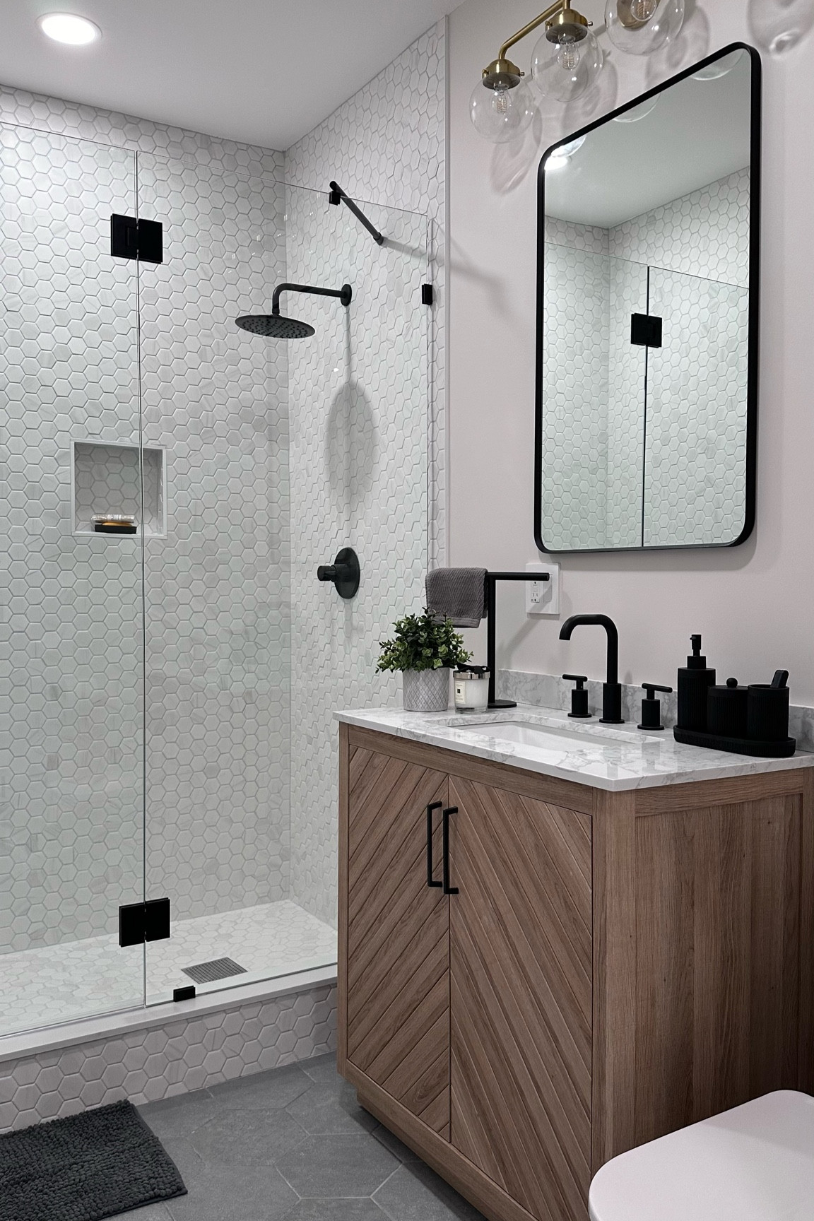 Here’s another bathroom renovation we recently completed at home. For this space, I wanted to create a balanced, contemporary look with cool-toned neutrals like gray and black. To add warmth, I incorporated a cool-toned wood vanity and complemented it with gold accents, including the light fixtures and picture frames (the frames are on the opposite wall and not visible in this shot)

#LTKHome