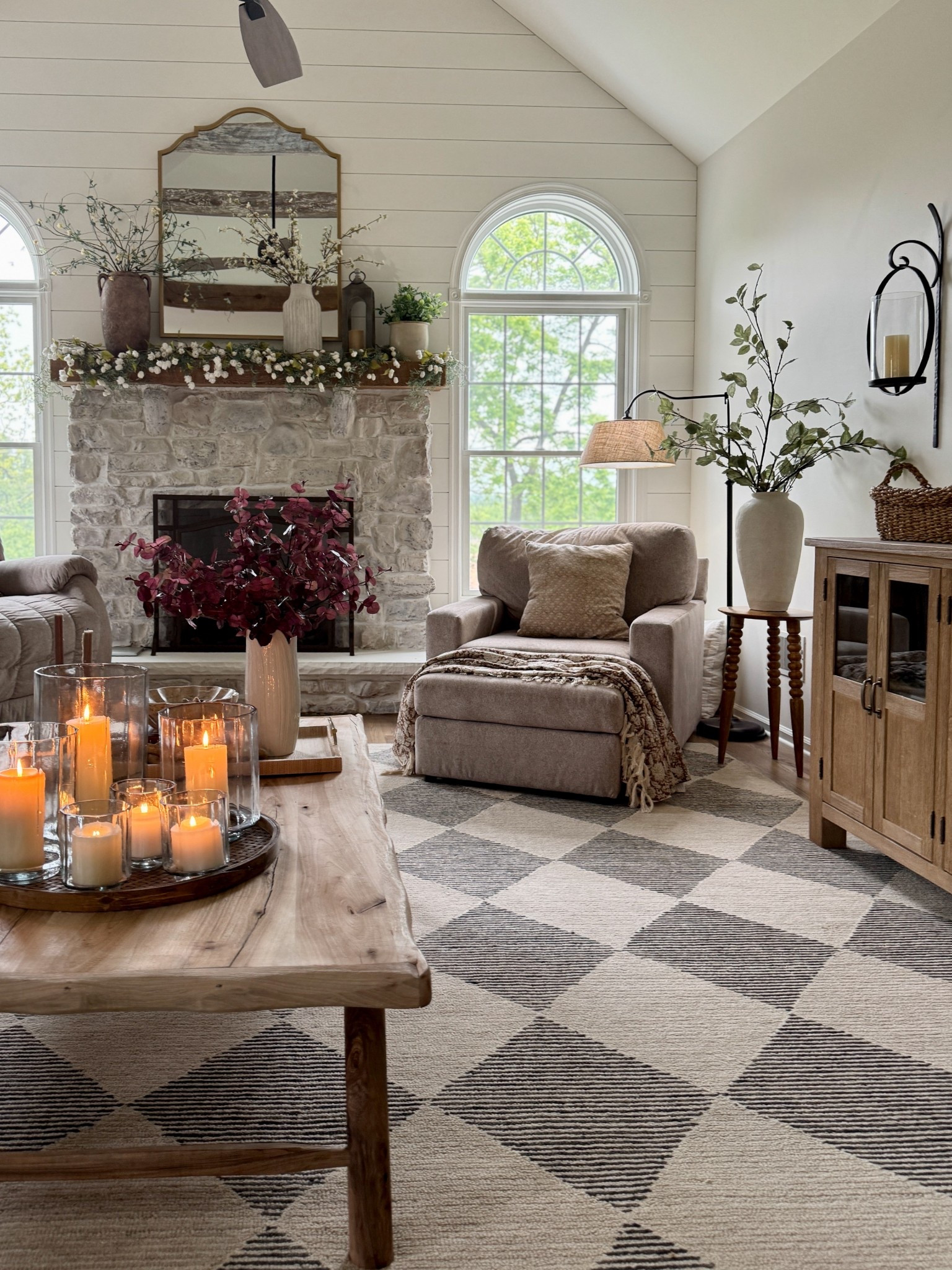 Beautiful hand made reclaimed wood coffee table. Neutral geometric rug. Glass hurricane candle holders in 3 sizes. Curved arm floor lamp with linen shade. Solid wood accent table. Faux cascading cream white hops florals on top of fireplace, handcrafted metal lantern, gold mirror, large faux sage stems, white vases, black and cream floral pillow covers, round wall sconces, solid wood buffet table  

#LTKMidsize #LTKHome