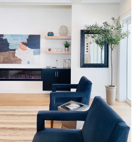 Cohesive Transitional Living Room Decor with blue velvet accent chairs, abstract painting, electric fireplace, black beveled mirror, 6 foot Olive tree and black floating cabinet.  #TransitionalLivingRoom

#LTKhome #LTKstyletip