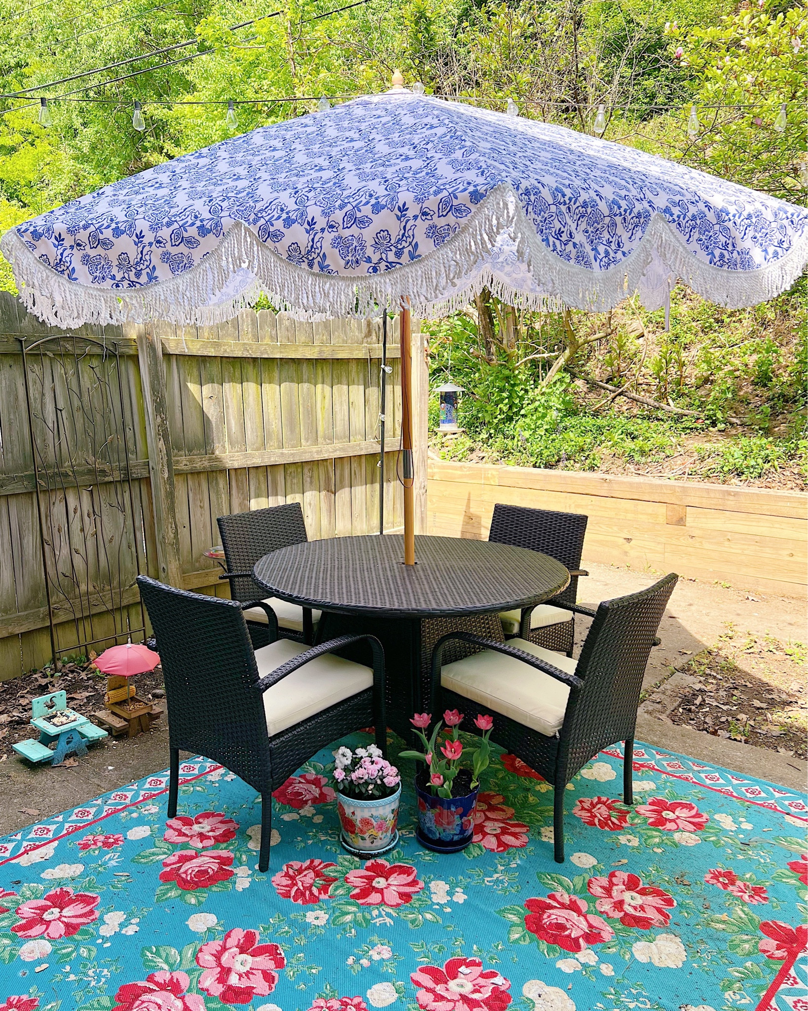 Four seat outdoor dining set with blue and white patio umbrella, floral print outdoor rug, blue and white flower pots, outdoor string lights, and squirrel feeder ☂️☀️🌸🐿️ patio furniture, patio decor, outdoor furniture, outdoor decor, planter pot, umbrella with fringe 

#LTKhome #LTKFind #LTKSeasonal