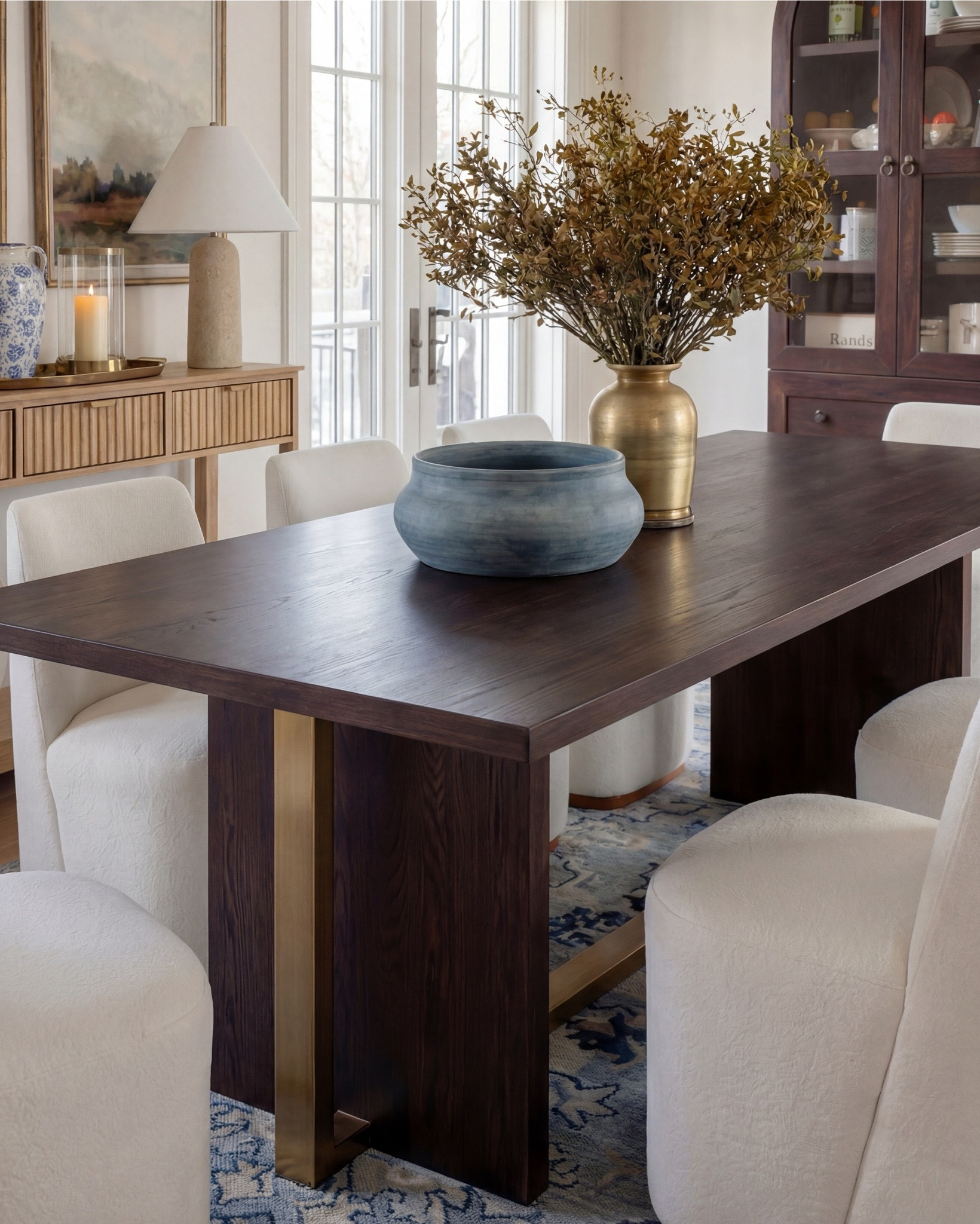 This dining room feels calm, intentional, and quietly elevated. The exposed wood beams warm up the space, while soft blues—on the ceiling and rug—bring in that serene, lived-in charm. The contrast between the dark wood table and the plush ivory chairs makes everything feel grounded yet refined.

The styling really sells it: a blue ceramic bowl centered on the table, a brass vase with organic branches for height, and layered decor along the sideboard that keeps the room from feeling too formal. It’s traditional at its core, but styled in a way that feels fresh and current.

Shop the Look:
• Dark wood rectangular dining table
• Curved ivory upholstered dining chairs (wood base)
• Blue ceramic decorative bowl (table centerpiece)
• Brass vase with dried branches
• Blue patterned area rug
• Light wood sideboard with fluted drawer detail
• Blue-and-white ceramic vase (sideboard)
• Neutral table lamp with white shade
• Stacked books + candle decor
• Framed landscape wall art (set of two)
• Dark wood arched china cabinet with glass doors
• White ceramic floor vase
• Exposed wood ceiling beams
• Soft blue ceiling paint
• Tall floor vase

#LTKhome #LTKsale #LTKstyletip