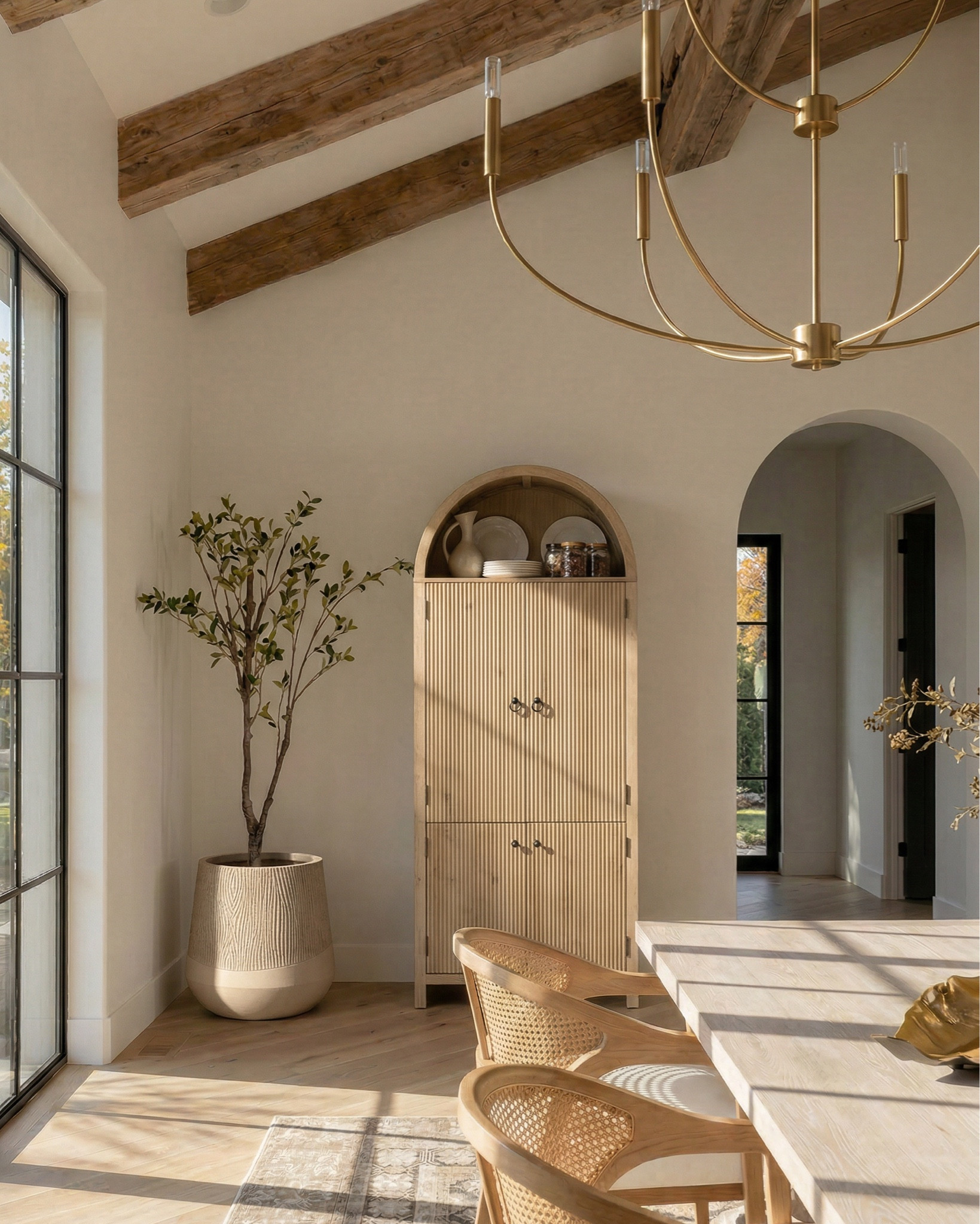 * Rectangular light wood dining table (traditional trestle base)
* Woven cane dining chairs (natural oak frame)
* Neutral vintage-style area rug (distressed pattern)
* Brass modern chandelier (linear / sculptural arms)
* Rustic exposed wood ceiling beams (reclaimed look)
* Large black-framed sliding glass doors (industrial style)
* Dark ceramic vase (handmade / organic texture)
* Dried floral arrangement (neutral stems)
* Sculptural brass decorative bowl
* Black ceramic candle holder (modern abstract form)
* White taper candle
* Small matte black decorative bowl
* Minimalist sculptural object (black accent piece)
* Light wood sideboard cabinet (fluted / ribbed detailing)
* Built-in arched niche cabinet (custom millwork look)
* Decorative pottery (neutral ceramic vases)
* Framed landscape wall art (classic / muted tones)
* Indoor olive tree (or faux olive tree)
* Neutral linen / textured textiles
* Warm light oak flooring
* Soft cream / off-white wall paint
* Arched doorway architectural detail


#LTKHome #LTKSaleAlert