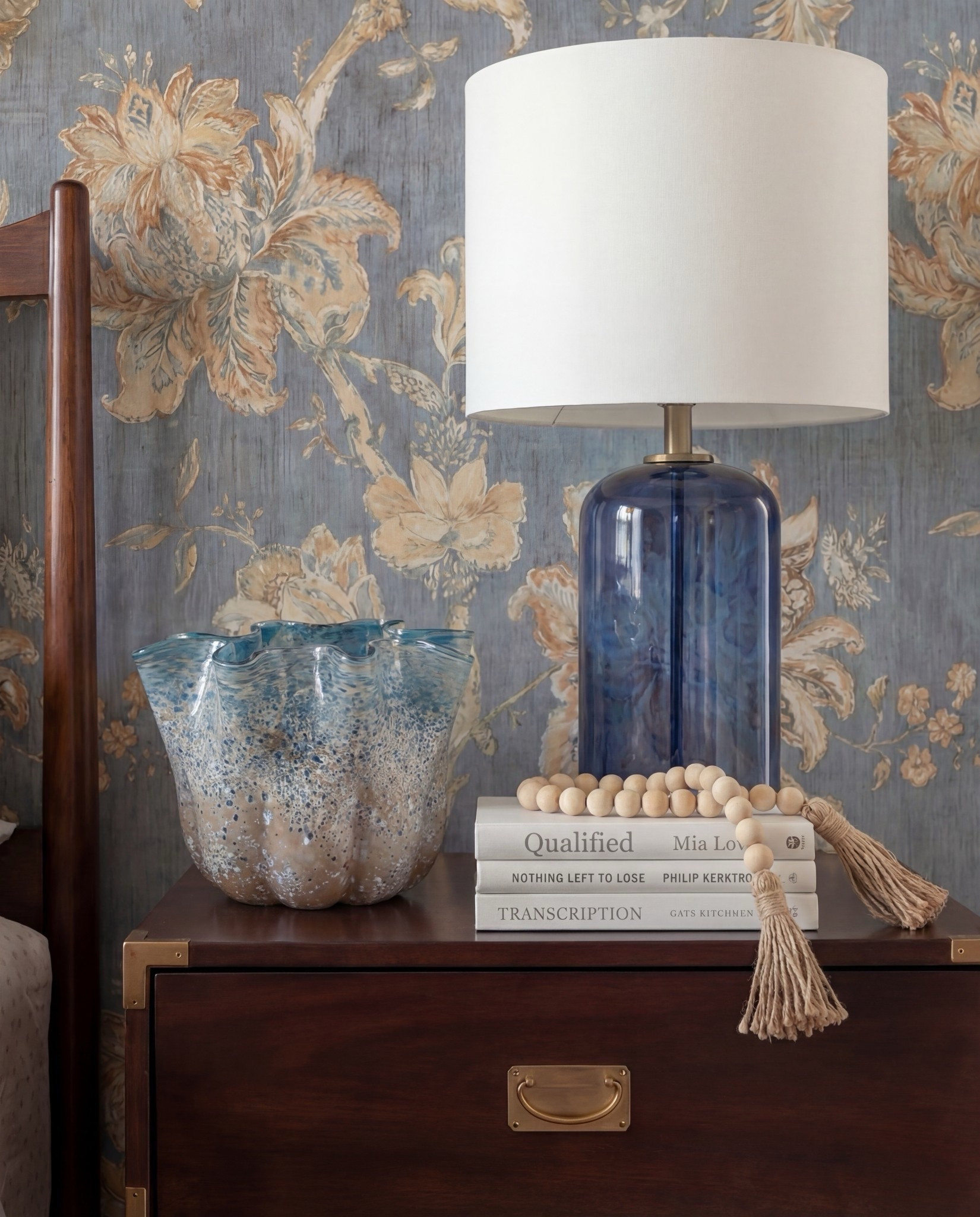 Shop the Look: Bedroom Refresh
• Warm-wood platform bed frame
• Vertical-channel upholstered headboard
• Gray duvet cover + layered sheet set
• Mixed blue + neutral accent pillows
• Oversized chunky knit throw blanket
• Shearling-style upholstered storage bench at the foot of the bed
• Pair of dark-wood campaign-style nightstands with brass hardware
• White drum-shade table lamps with blue glass bases
• Blue decorative bowls
• Bead garland décor
• Stack of books (nightstand styling)
• Framed oversized floral artwork above the bed
• Blue floral wallpaper (full wall + ceiling)
• Exposed wood ceiling beams
• Blue patterned area rug
• Window bench with plaid/tan accent pillows

#LTKHome #LTKSaleAlert #LTKSpringSale