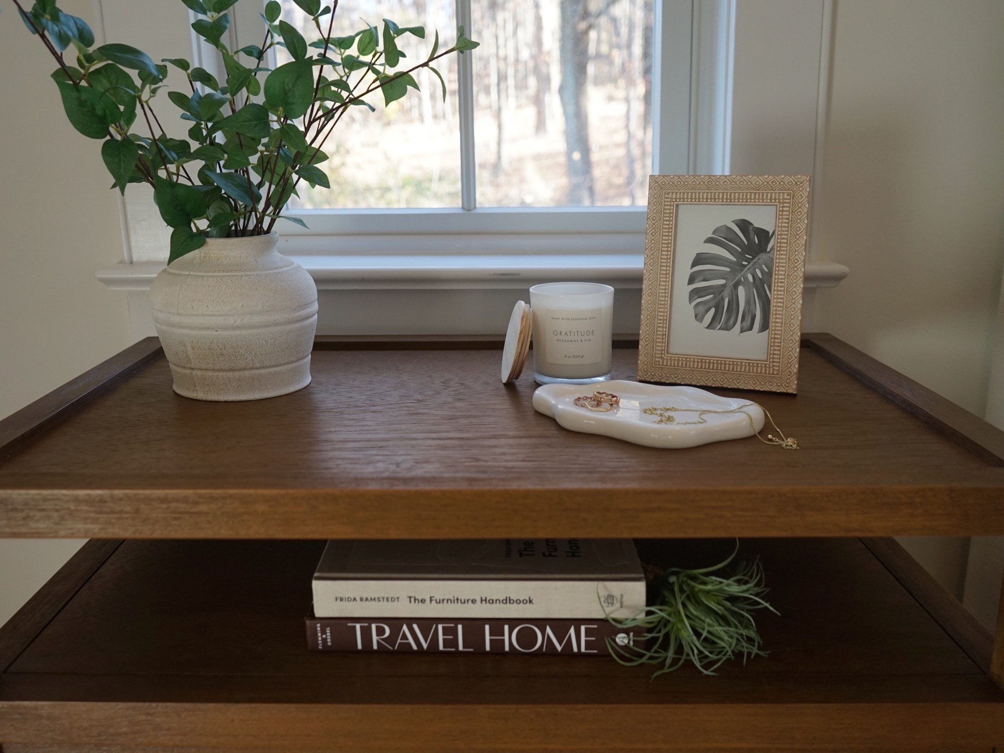 A close-up of her side of the nightstand showcases a beautifully styled vignette with a delicate jewelry tray resting atop the rich wood surface. Soft lighting from a nearby sconce casts a warm glow, highlighting the nightstand’s natural grain and the serene, lived-in charm of the bedroom. 