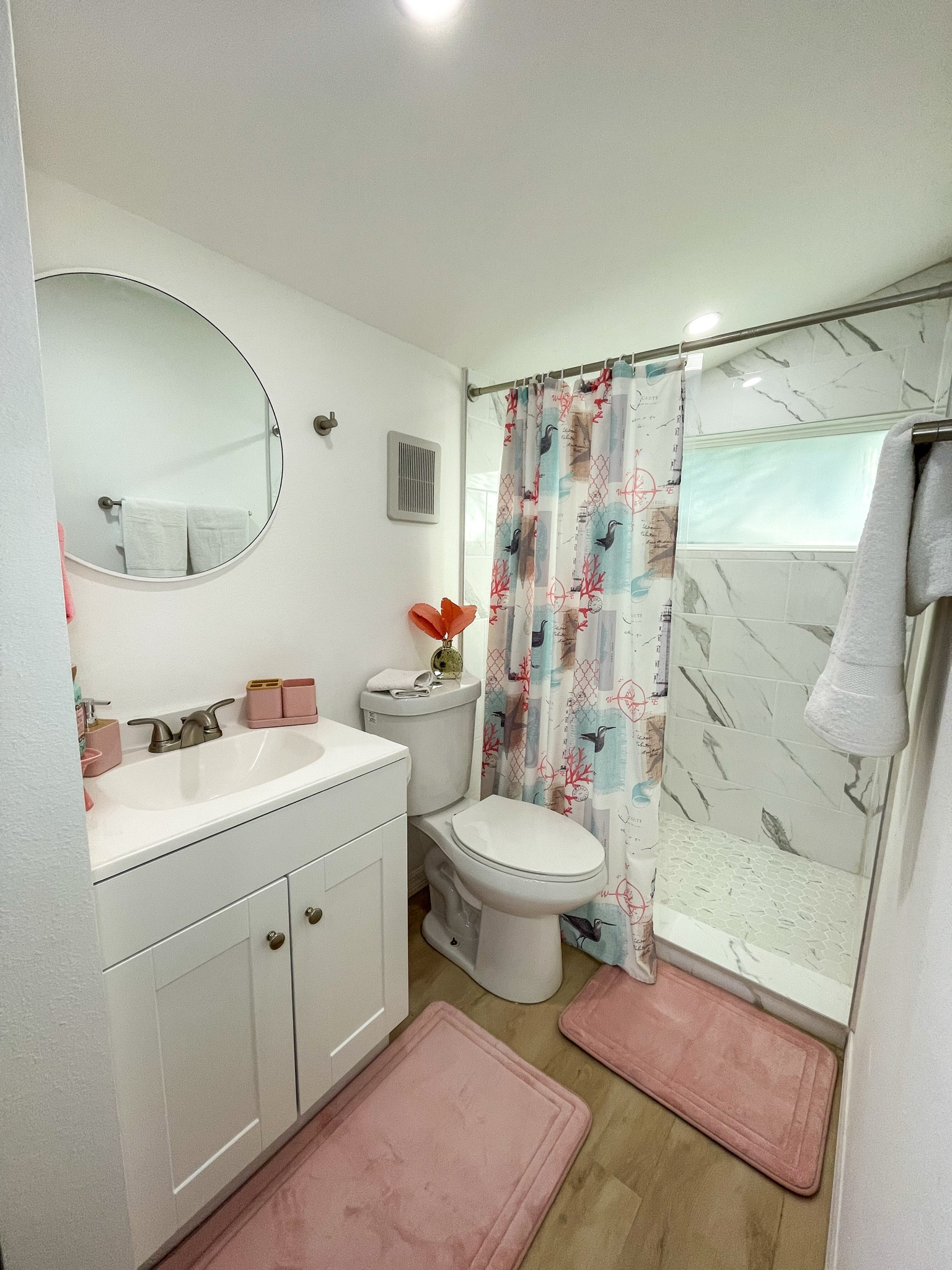 Clean, bright bathroom with pink mats and coastal touches.